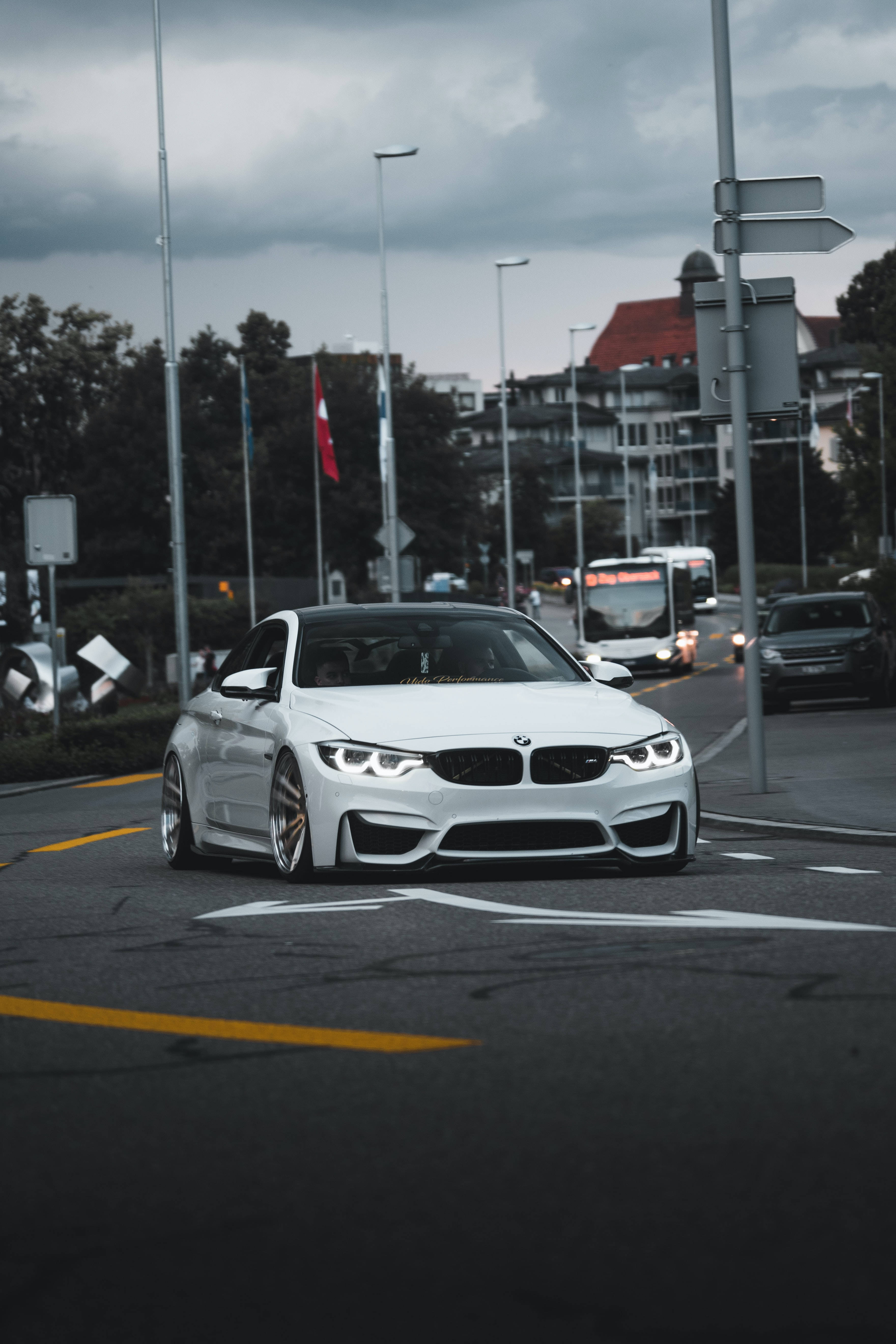 Bmw M Series 桌布 壁紙 — 一輛時尚的白色BMW M4雙門轎跑車，車頭燈發光，在多雲的天空下主宰著潮濕的城市街道。