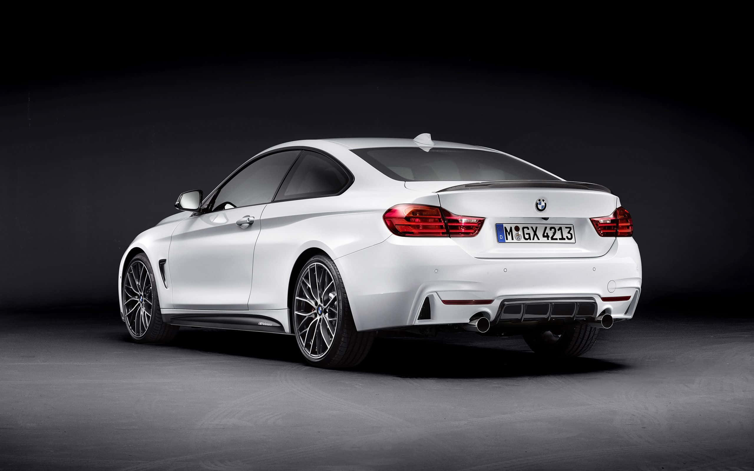 Bmw 4 Series 桌布 壁紙 — 一輛時尚的白色BMW M4雙門轎跑車，從後方四分之三角度拍攝，背景為昏暗的攝影棚，燈光效果戲劇化。