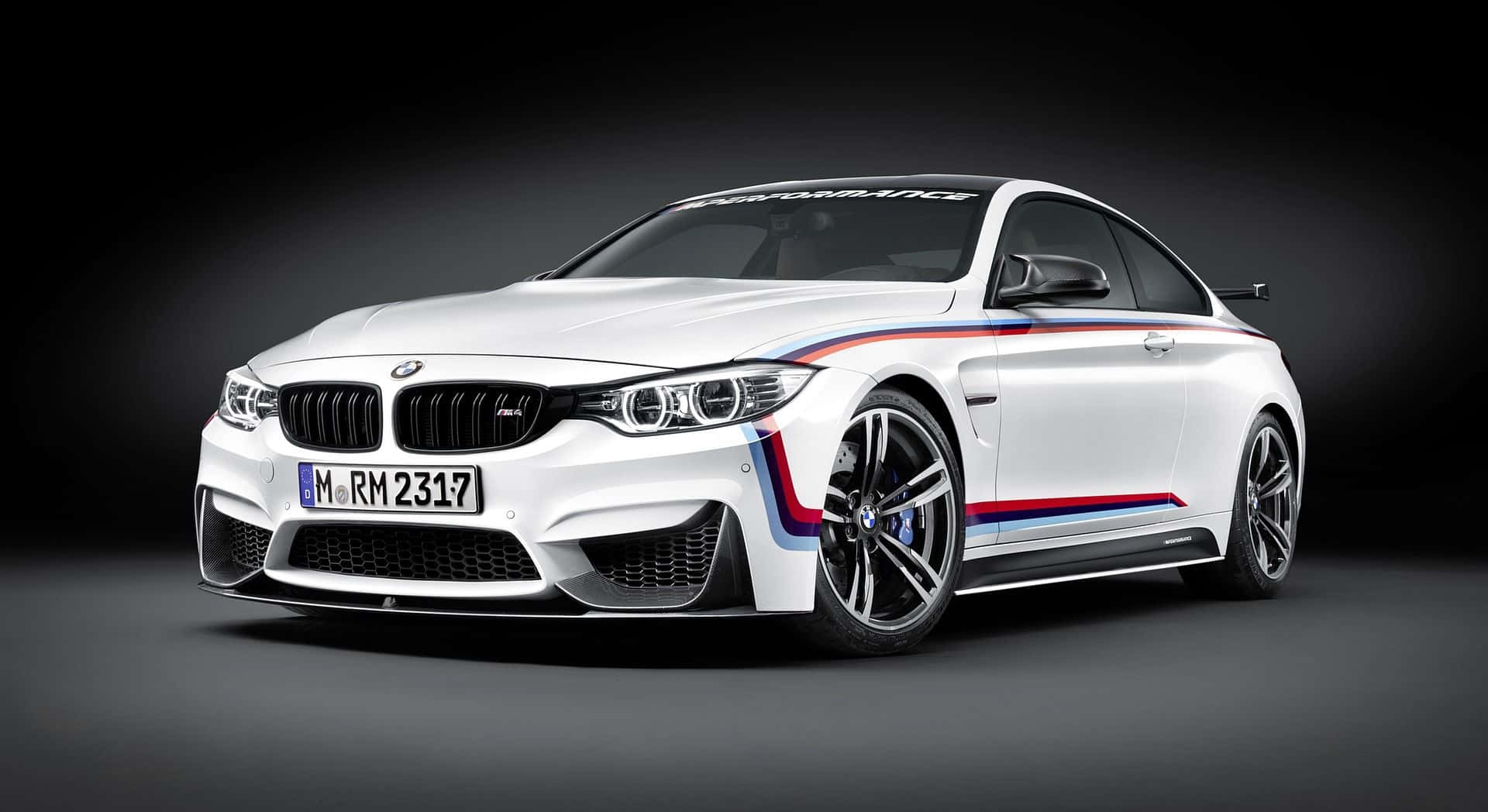 BMW 動圖 桌布 壁紙 — 一輛時尚的白色BMW M4雙門轎跑車，帶有紅色、藍色和黑色賽車條紋，在深色工作室背景下展示。