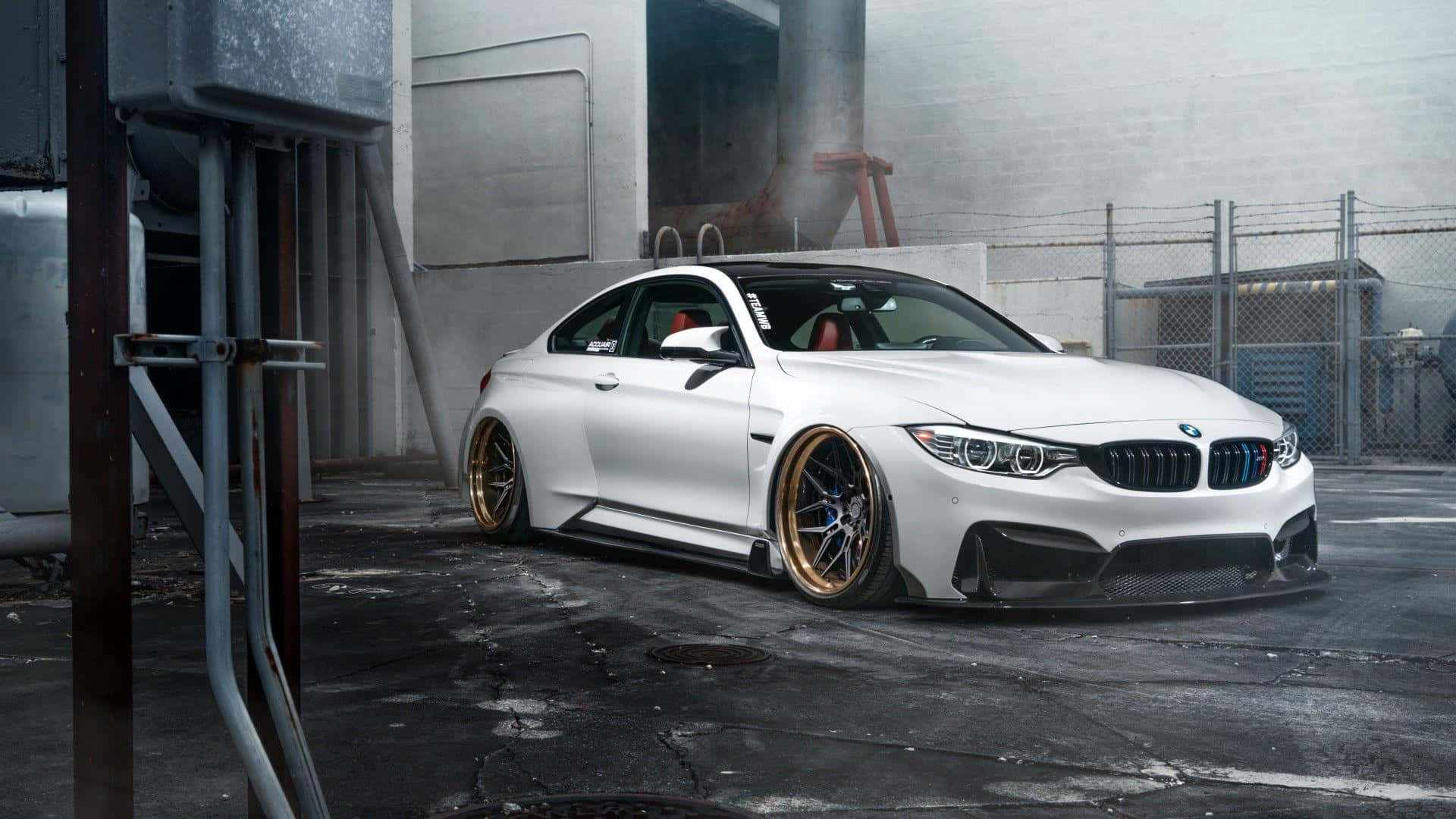 Bmw Cars 桌布 壁紙 — 一輛時尚的白色BMW M4雙門轎跑車搭配金色輪圈，停放在有混凝土牆和金屬圍欄的工業車庫中。
