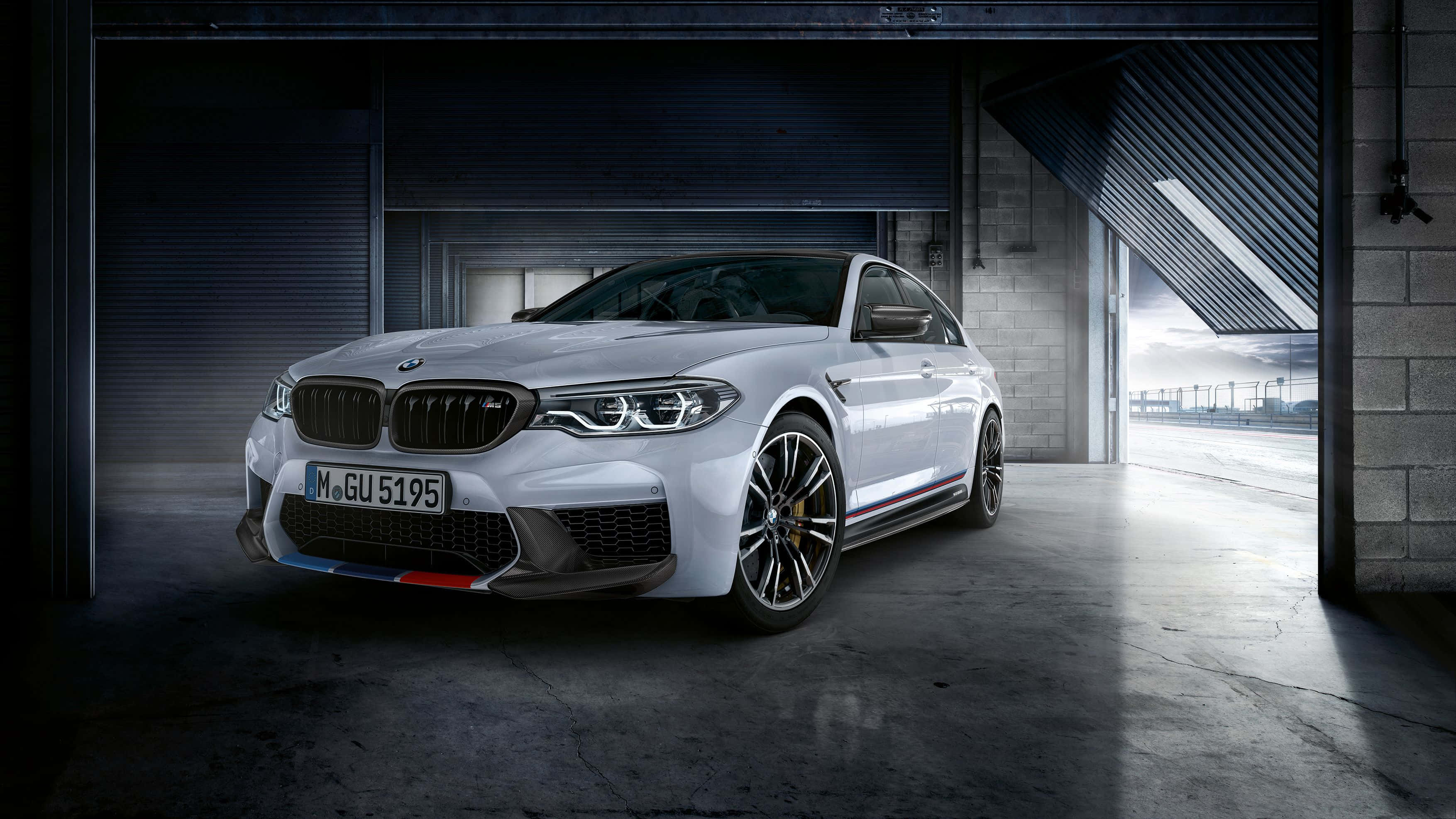 Bmw M5 桌布 壁紙 — 一輛時尚的白色BMW M5停放在昏暗的工業車庫中，戲劇性的燈光凸顯其侵略性設計。