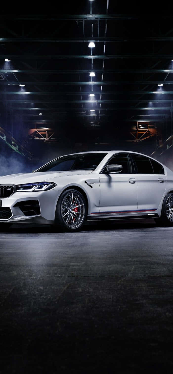 桌布 壁紙 — 一輛時尚的白色BMW M5跑車在黑暗的工業車庫中，在戲劇性的聚光燈和煙霧效果下閃閃發光。