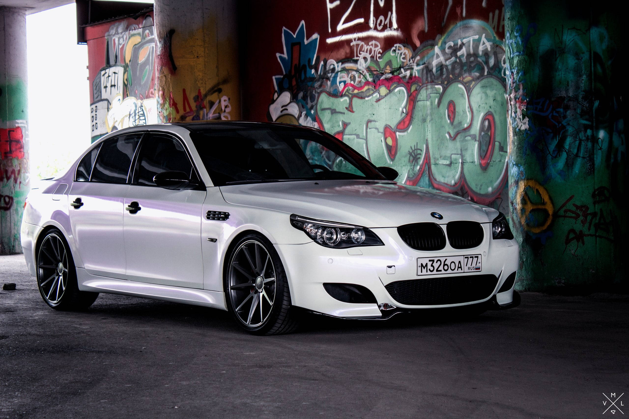 BMW 動圖 桌布 壁紙 — 一輛時尚的白色BMW M5運動轎車停放在佈滿塗鴉的城市高架橋下，光線效果極具戲劇性。