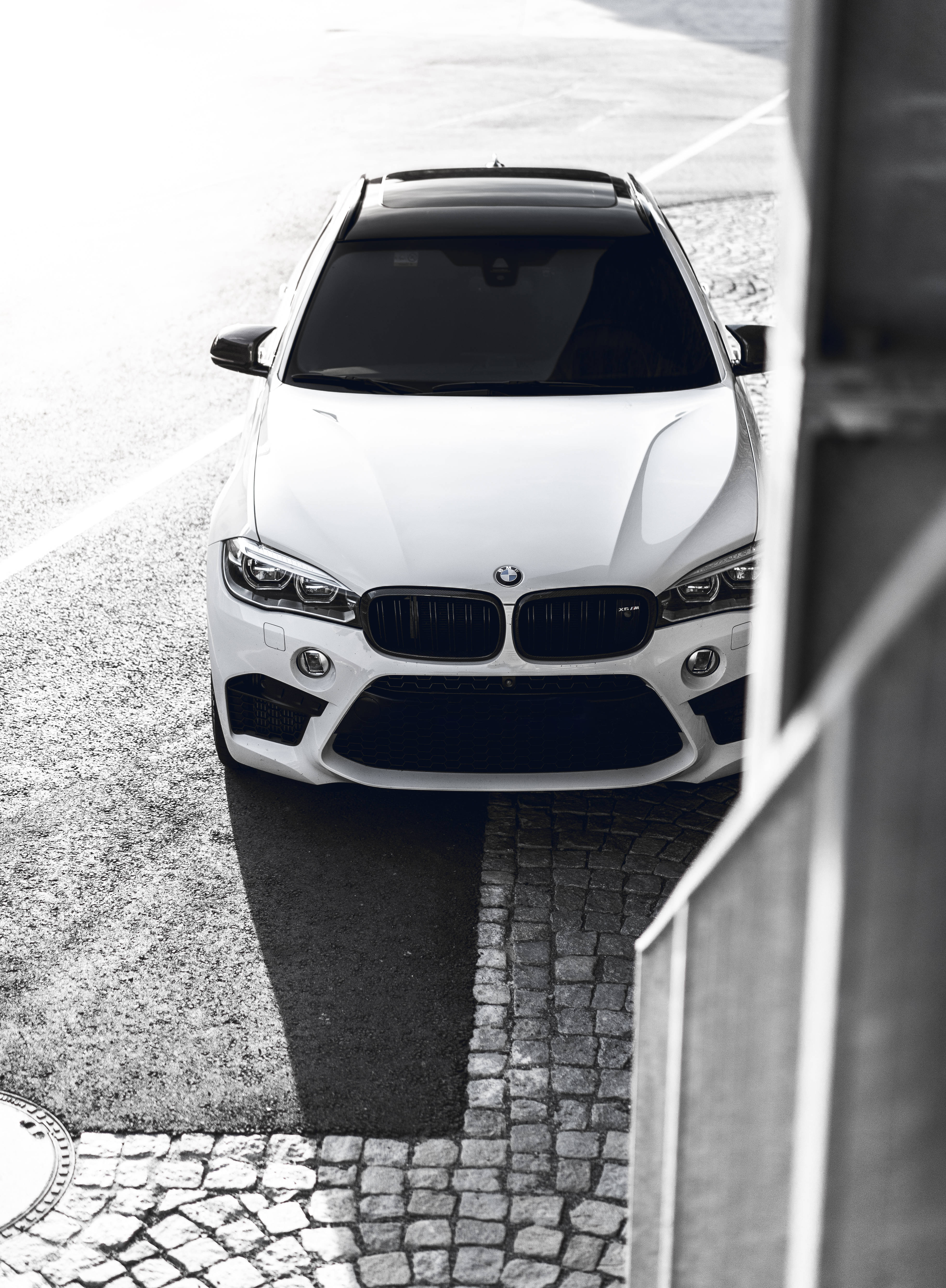 m 桌布 壁紙 — 一輛時尚的白色BMW SUV從上方俯瞰在鵝卵石街道上，帶有強烈陰影。