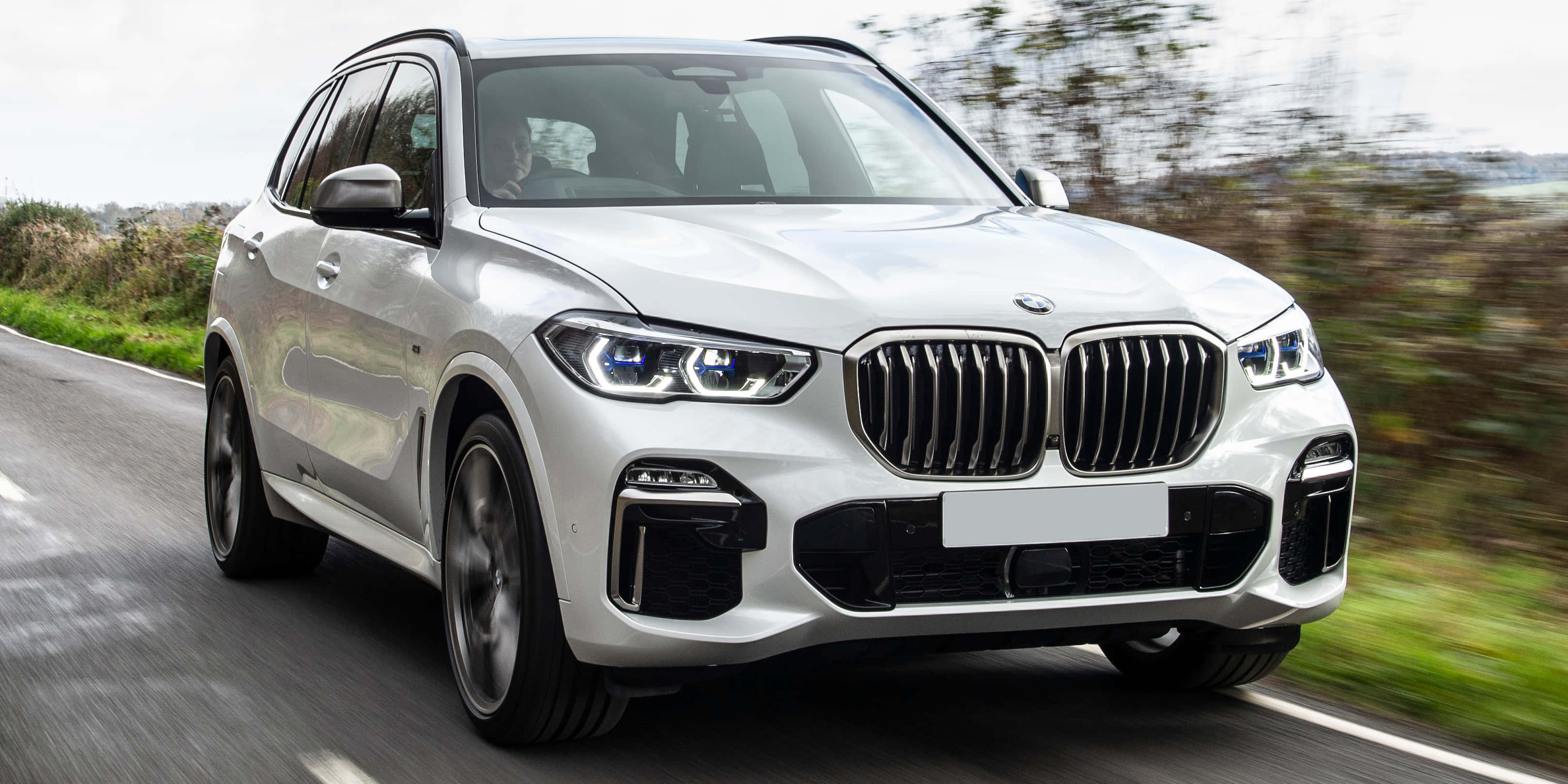 Bmw X5 桌布 壁紙 — 一輛時尚的白色BMW X5 SUV在蜿蜒的道路上疾馳，模糊的綠色植物呼嘯而過。