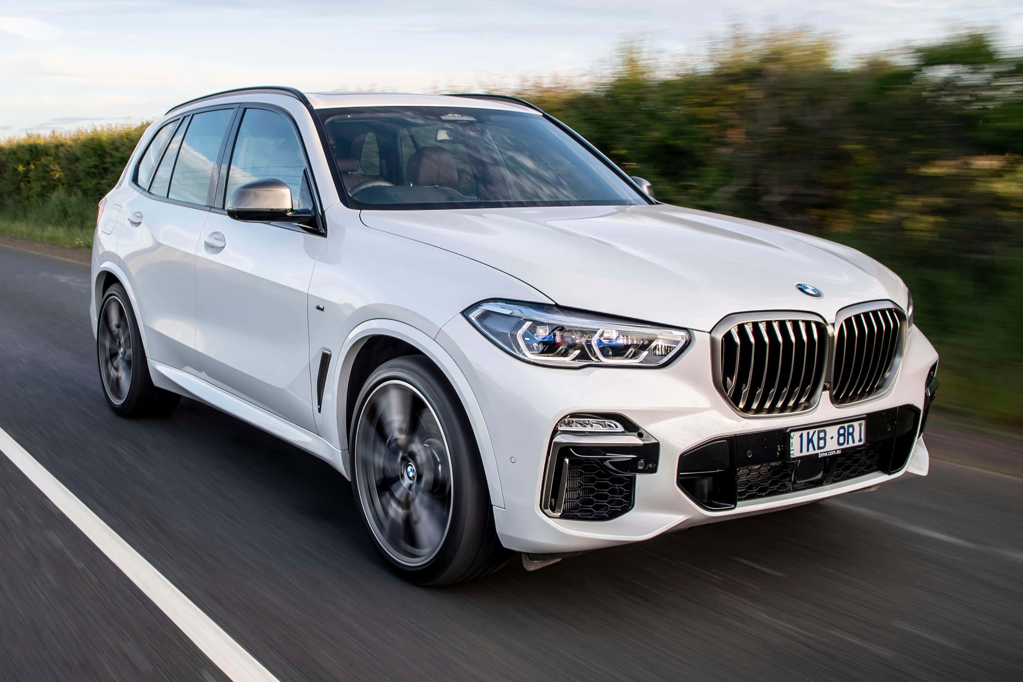 Bmw X5 桌布 壁紙 — 一輛時尚的白色BMW X5 SUV在鄉村道路上飛馳，背景是模糊的綠色植物。