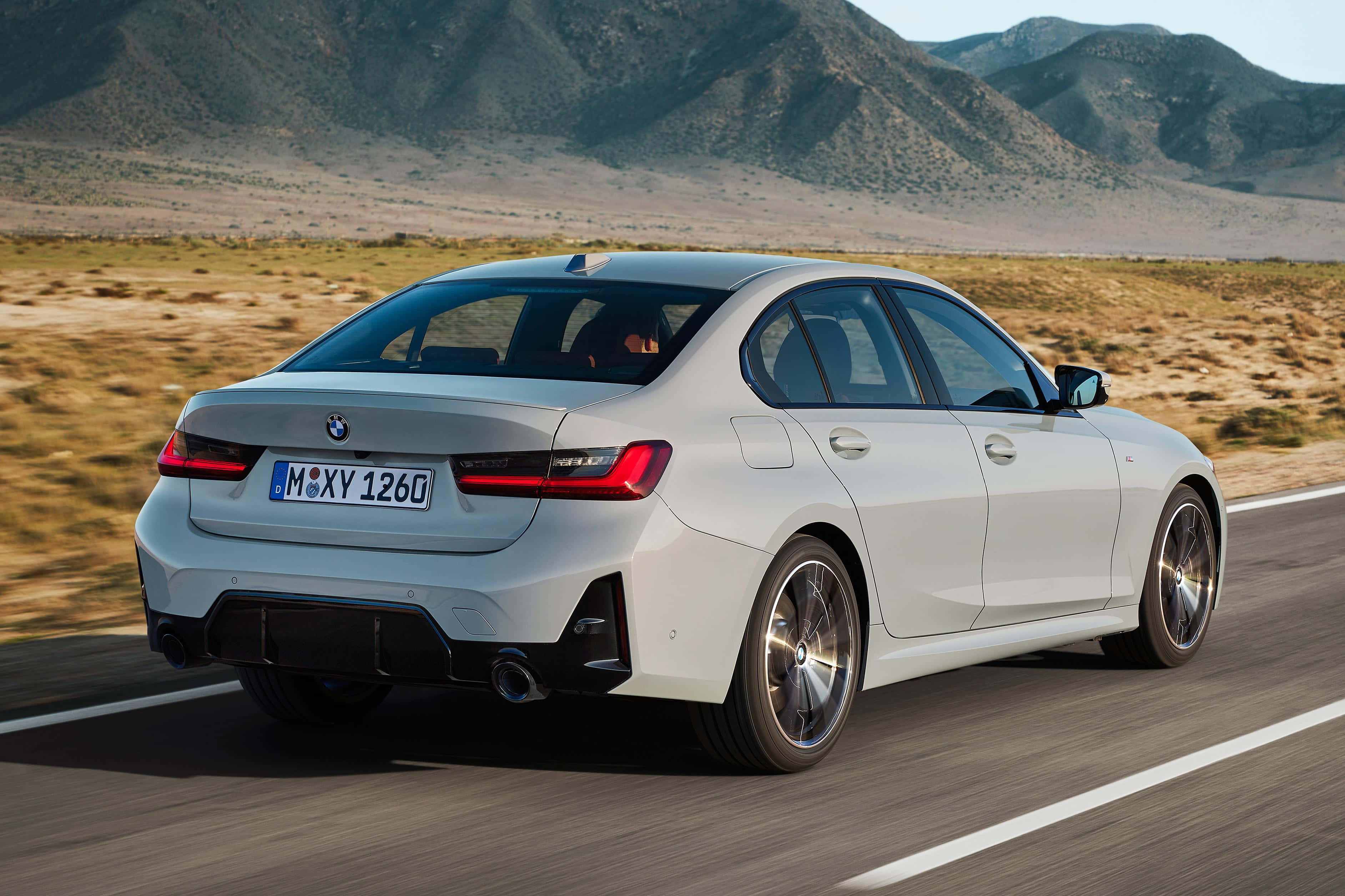 Bmw 3 Series 桌布 壁紙 — 一輛時尚的白色BMW轎車在明亮的日光下行駛在沙漠公路上，背景是崎嶇的山脈。