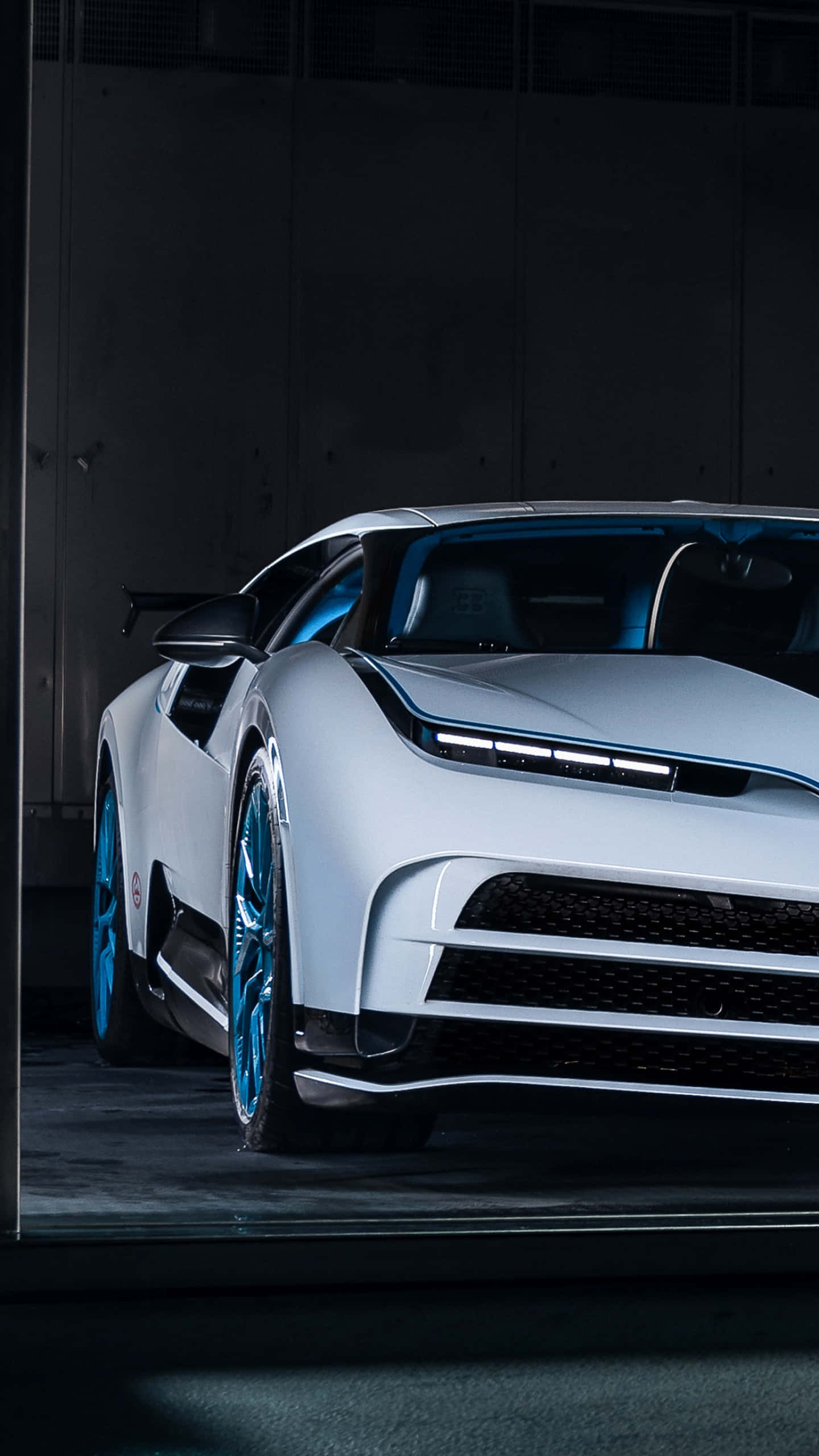 Bugatti Phone 桌布 壁紙 — 一輛時尚的白色Bugatti超跑，帶有發光的藍色飾邊和車輪，在黑暗的工業車庫中被戲劇性地照亮。