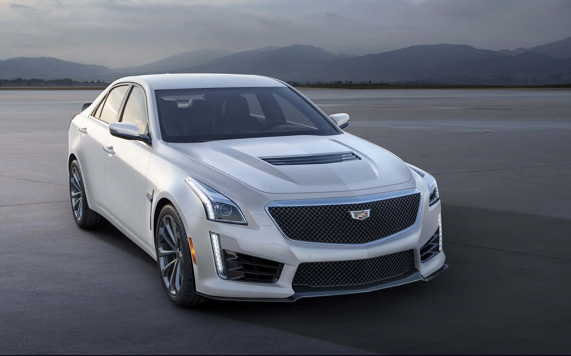 Cadillac Cts 桌布 壁紙 — 一輛時尚的白色Cadillac CTS-V運動轎車停放在廣闊的混凝土場地上，遠山在陰天之下。