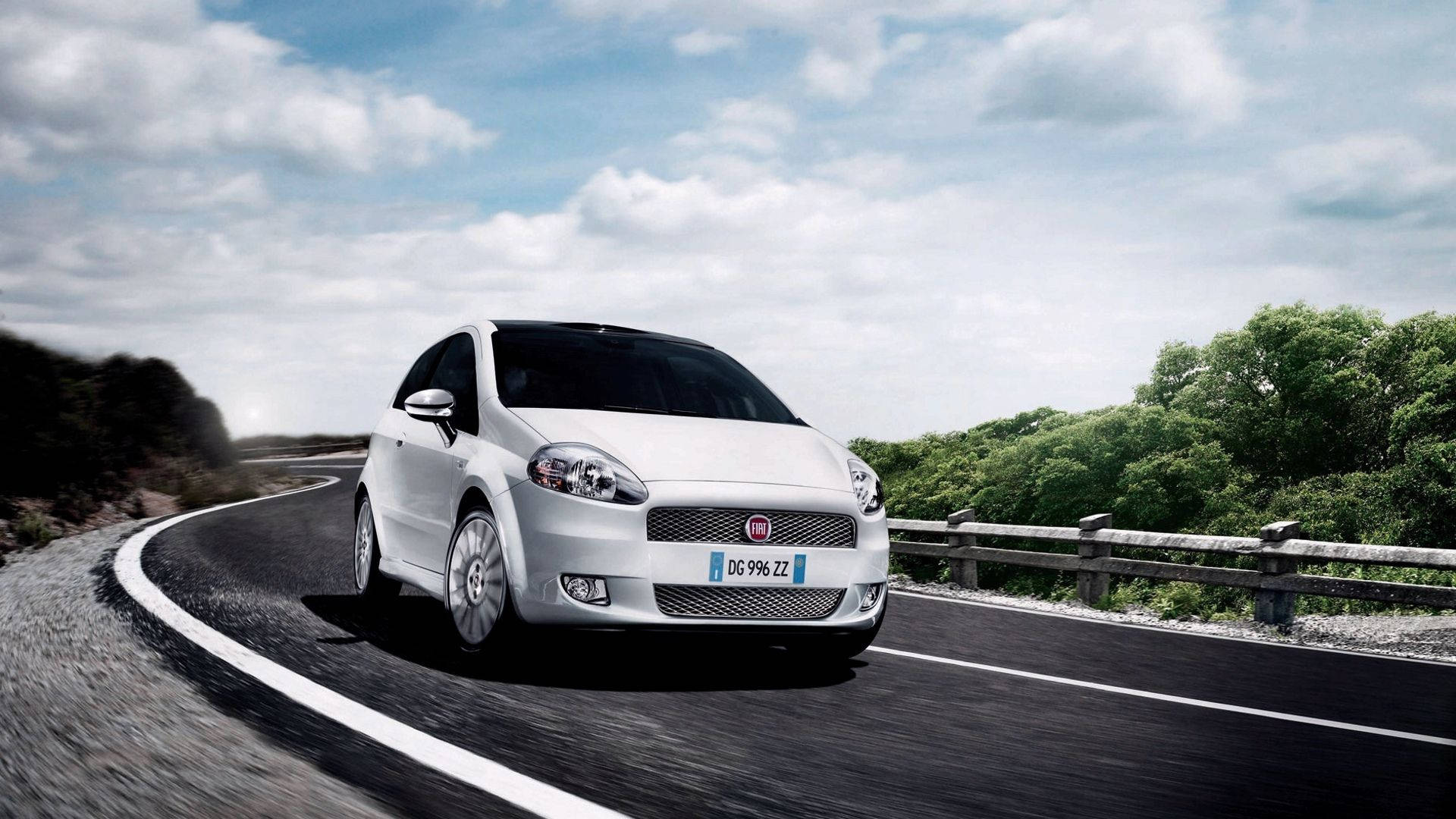 Fiat 桌布 壁紙 — 一輛時尚的白色Fiat Punto在部分多雲的天空下行駛在一條蜿蜒的瀝青路上，兩旁是茂密的綠樹。