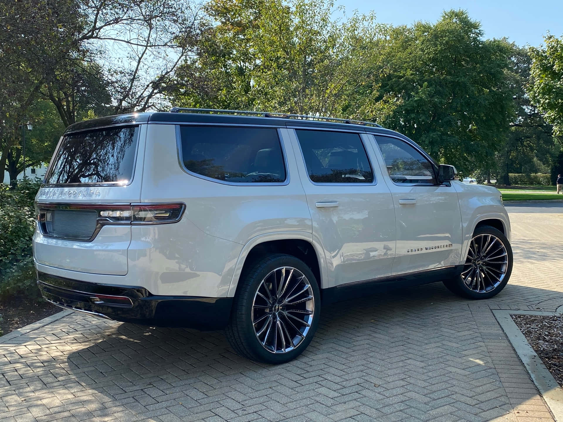 Jeep Wagoneer 桌布 壁紙 — 一輛時尚的白色GMC Yukon Denali SUV停放在陽光普照的磚砌車道上，周圍環繞著茂密的綠樹。