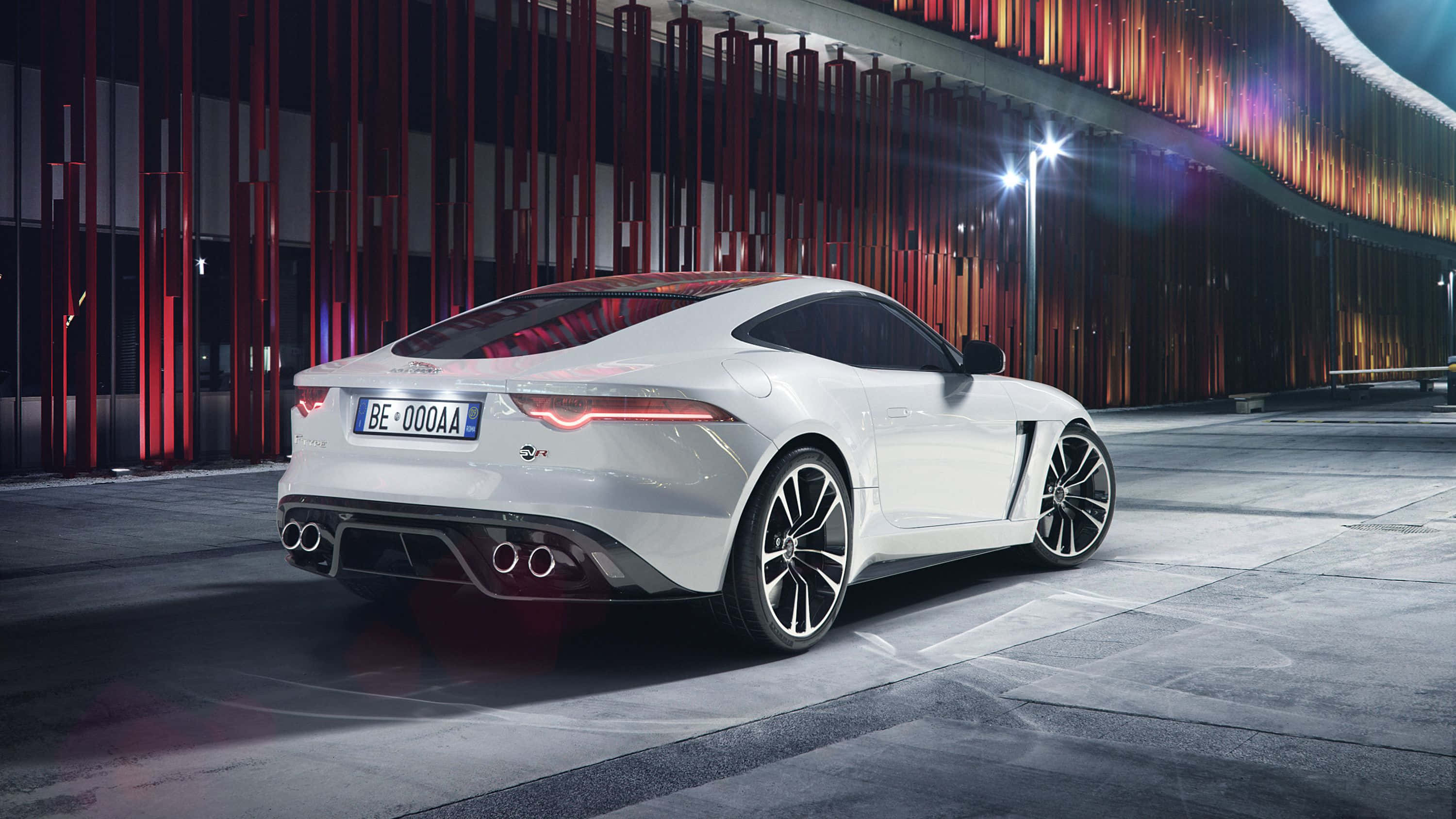 桌布 壁紙 — 一輛時尚的白色Jaguar F-Type跑車在夜間霓虹燈下，以現代紅黑建築背景為襯，閃閃發光。