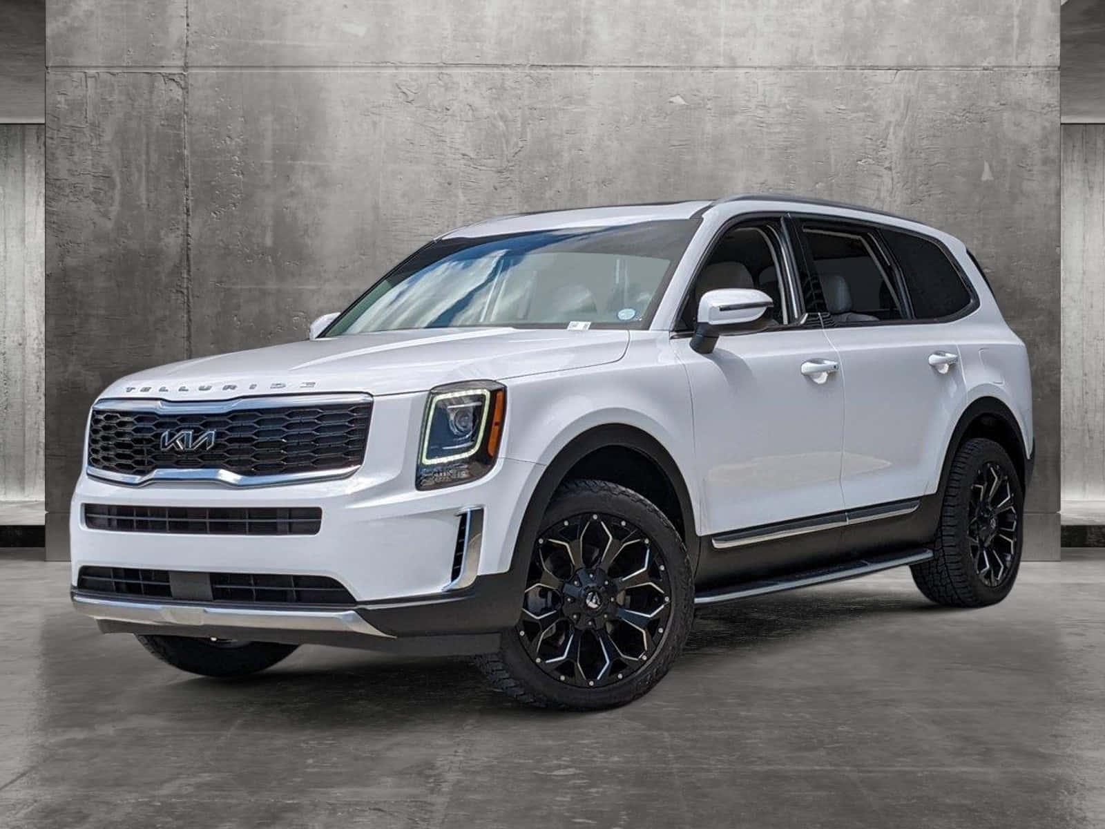 Kia Telluride 桌布 壁紙 — 一輛時尚的白色Kia Telluride SUV搭配黑色輪圈，在極簡主義工作室環境中，倚著紋理混凝土牆擺好姿勢。