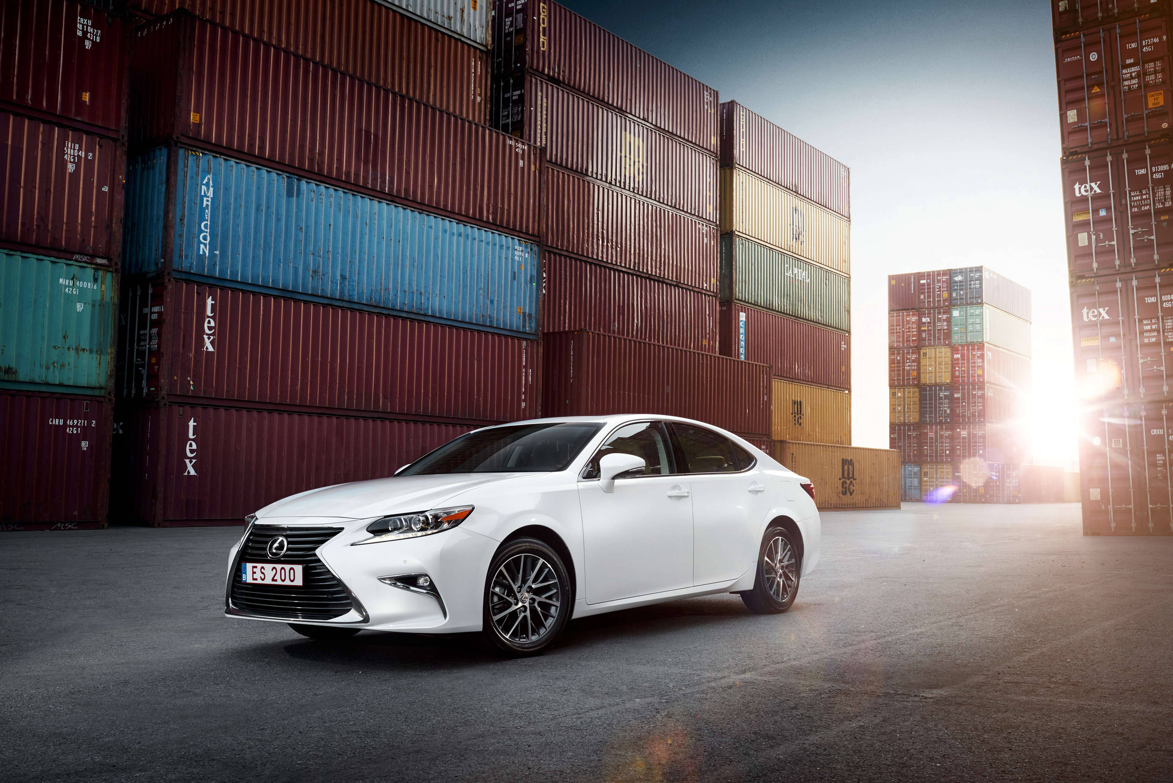 lexus iPhone 桌布 壁紙 — 一輛時尚的白色Lexus房車停放在色彩繽紛的高聳貨櫃之間，在明亮的陽光照射下。
