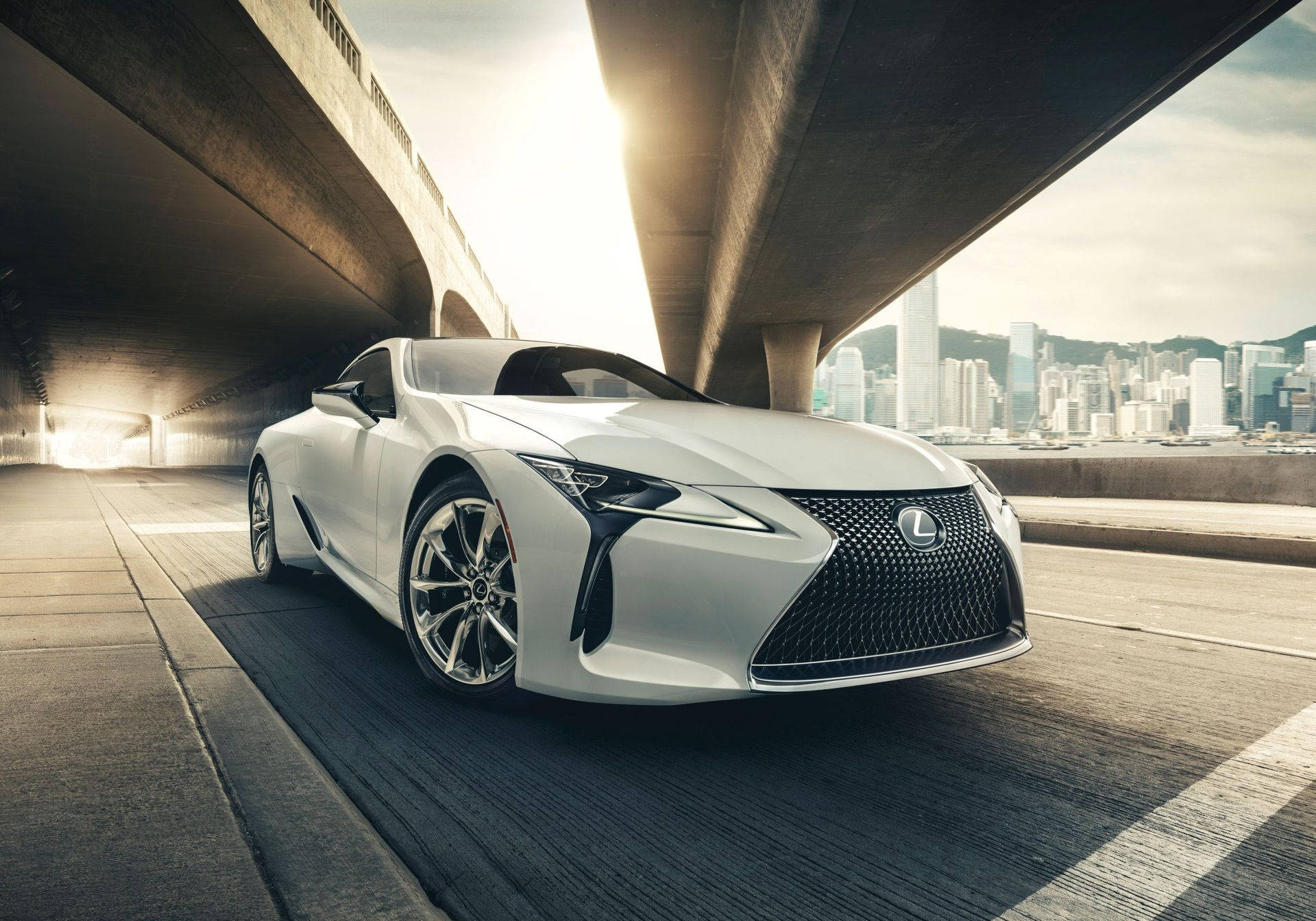 Lexus 標誌 桌布 壁紙 — 一輛時尚的白色Lexus跑車在混凝土高架橋下行駛，背景是閃爍的城市天際線。