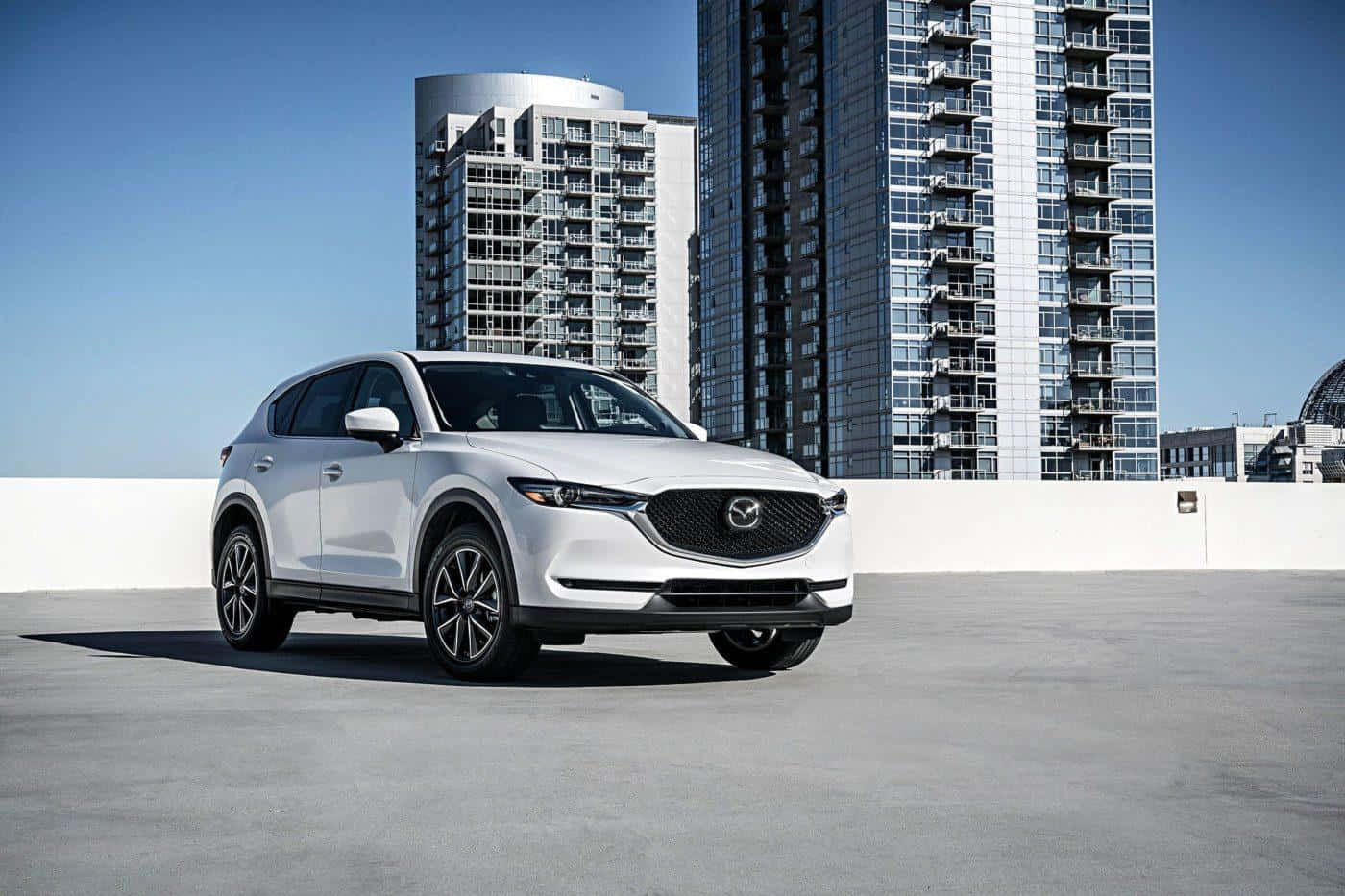 Mazda Cx-5 桌布 壁紙 — 一輛時尚的白色Mazda CX-5 SUV停放在屋頂上，背後是現代化的玻璃摩天大樓，在清澈的藍天下高聳入雲。