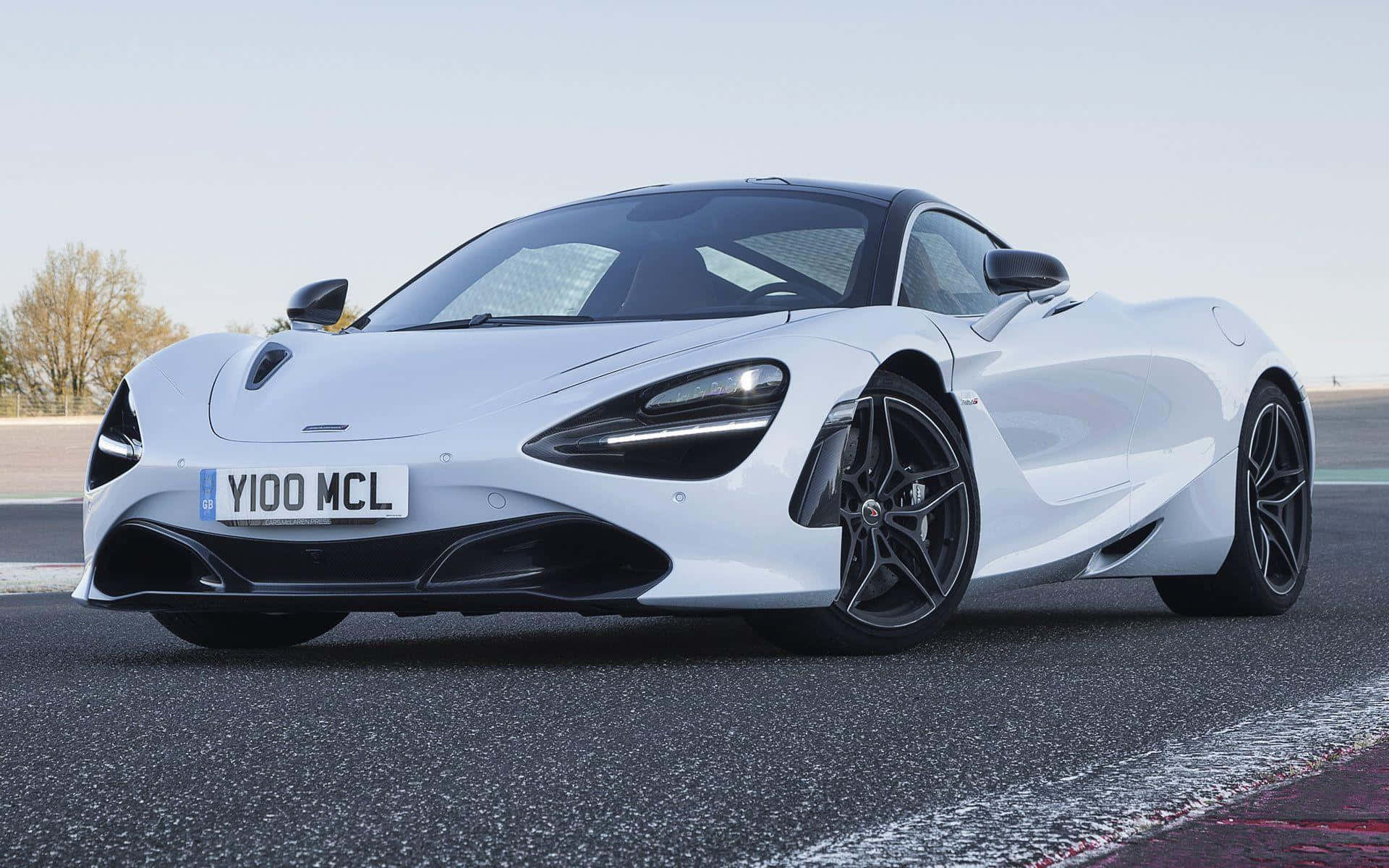 Mclaren 720s 桌布 壁紙 — 一輛時尚的白色McLaren 720S跑車，帶有黑色飾件，停在晴朗天空下的瀝青賽道上。