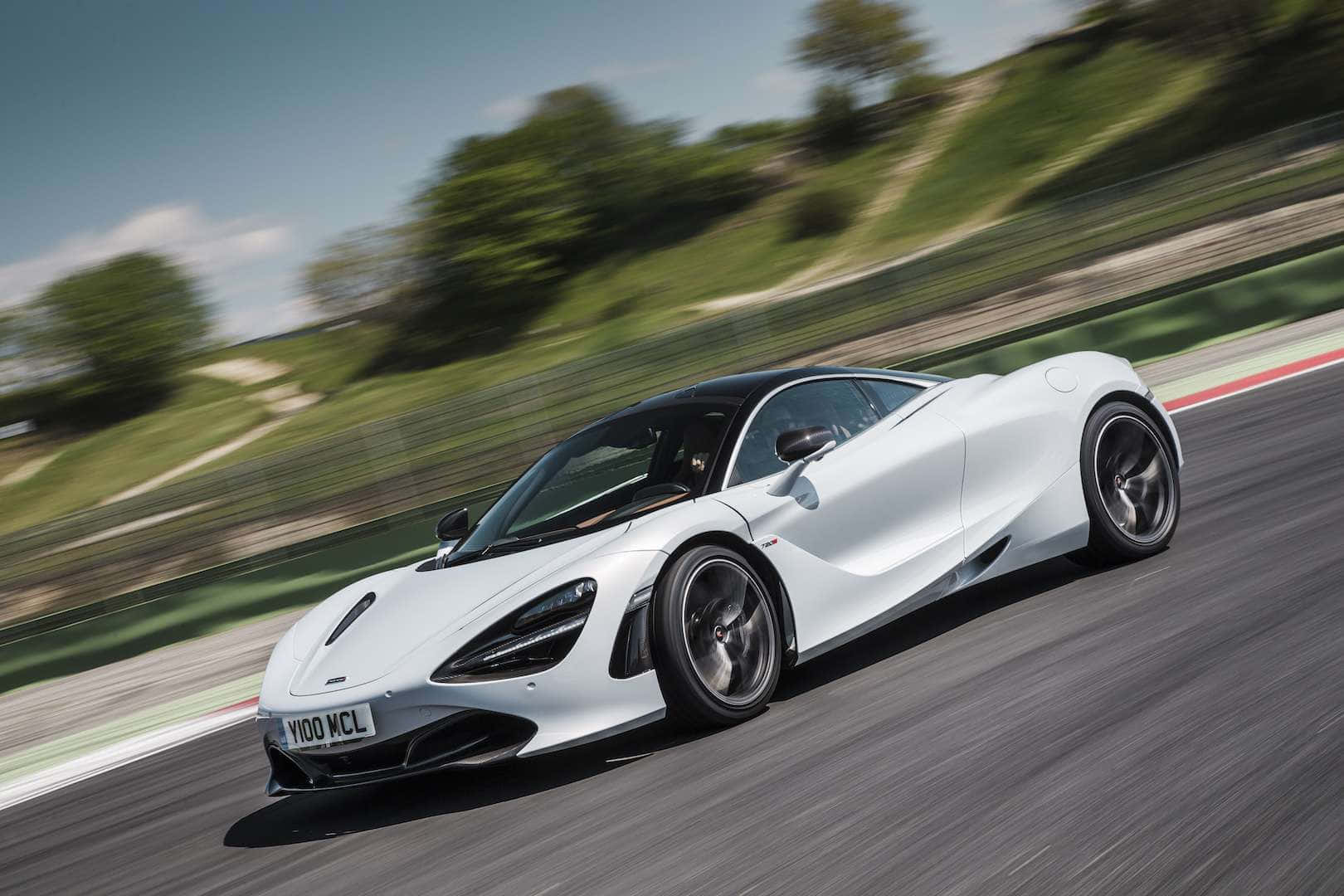 麥拉倫 720S 桌布 壁紙 — 一輛時尚的白色McLaren 720S在賽道上奔馳，背景是模糊的綠色山丘，頭上是晴朗的藍天。