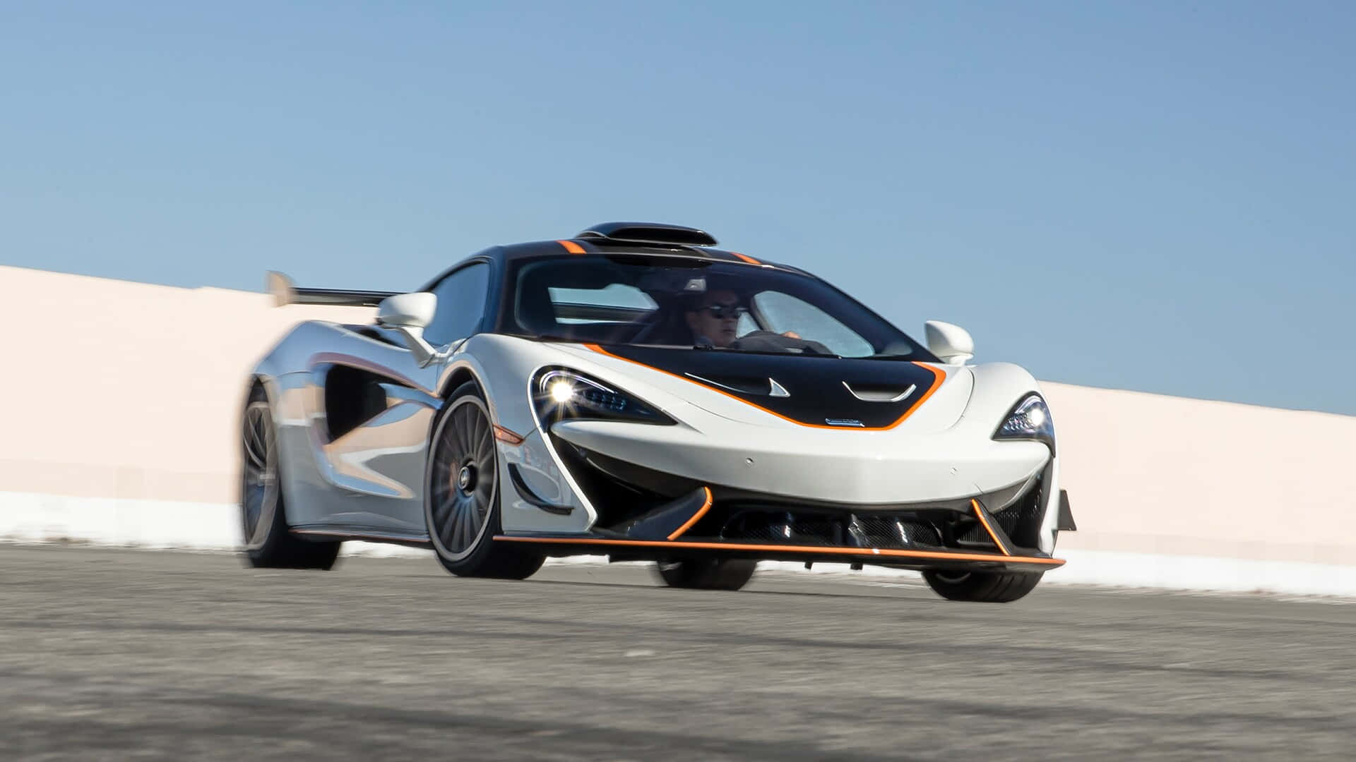 Mclaren 620r 桌布 壁紙 — 一輛時尚的白色McLaren超級跑車帶有橙色點綴，在晴朗的藍天下沿著賽道飛馳。