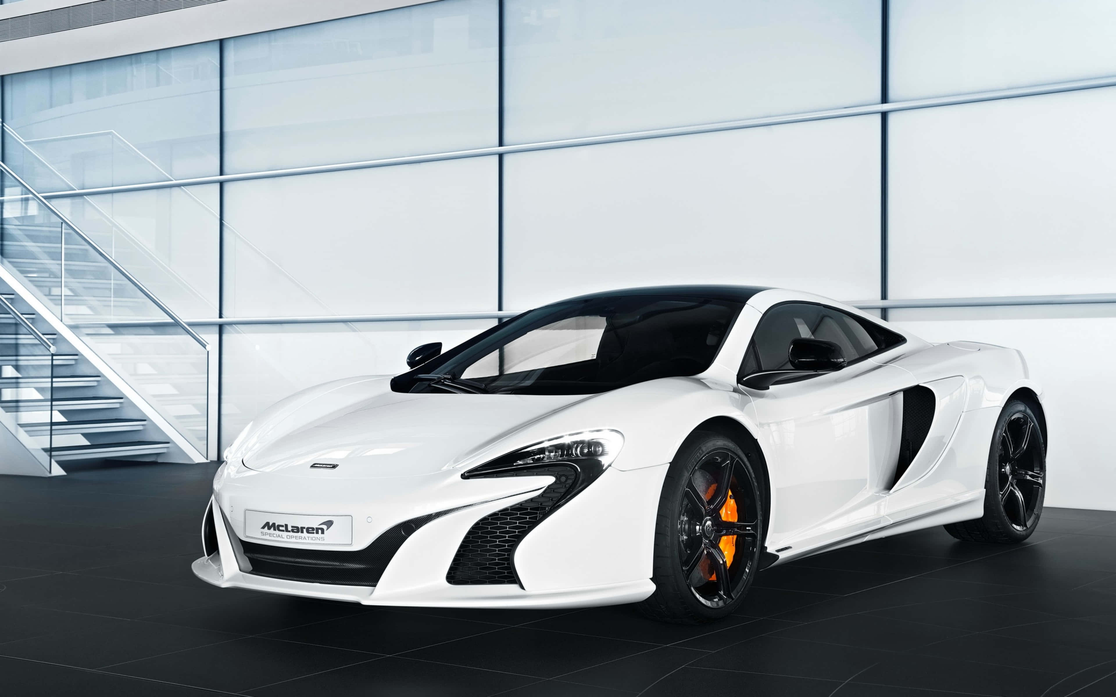 Cool Mclaren 桌布 壁紙 — 一輛時尚的白色McLaren跑車，帶有黑色飾件和橙色制動卡鉗，在現代玻璃牆陳列室中展示。