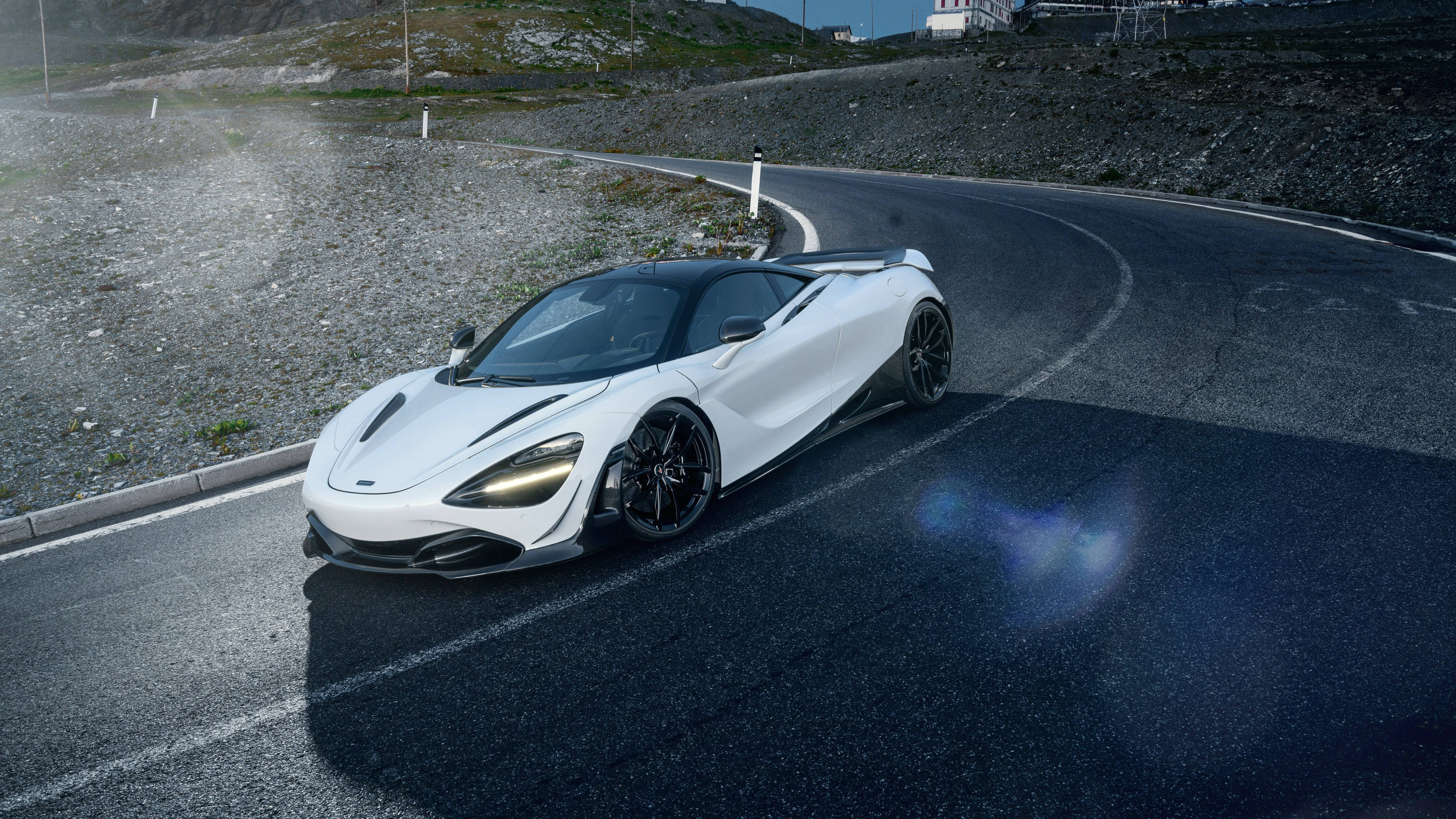 Mclaren 720s 桌布 壁紙 — 一輛時尚的白色McLaren跑車在晴朗的藍天下行駛在蜿蜒的山路上。