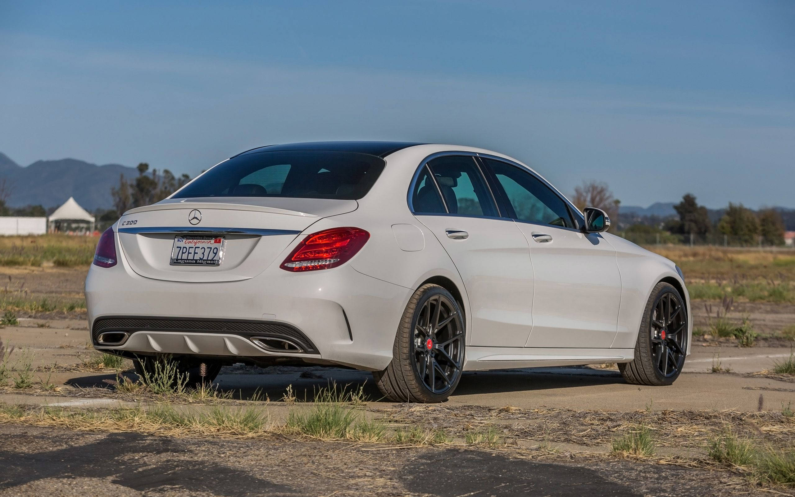 Mercedes Benz C300 桌布 壁紙 — 一輛時尚的白色Mercedes C63 AMG轎車，配備黑色輪圈，停在龜裂的柏油路上，天空湛藍清澈。