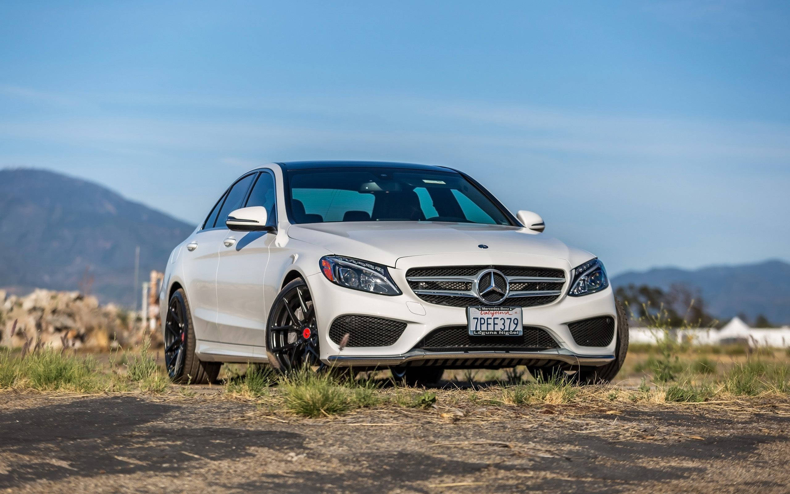 Mercedes Benz C300 桌布 壁紙 — 一輛時尚的白色Mercedes-AMG C63停泊在塵土飛揚的路邊，背景是山脈，天空清澈湛藍。