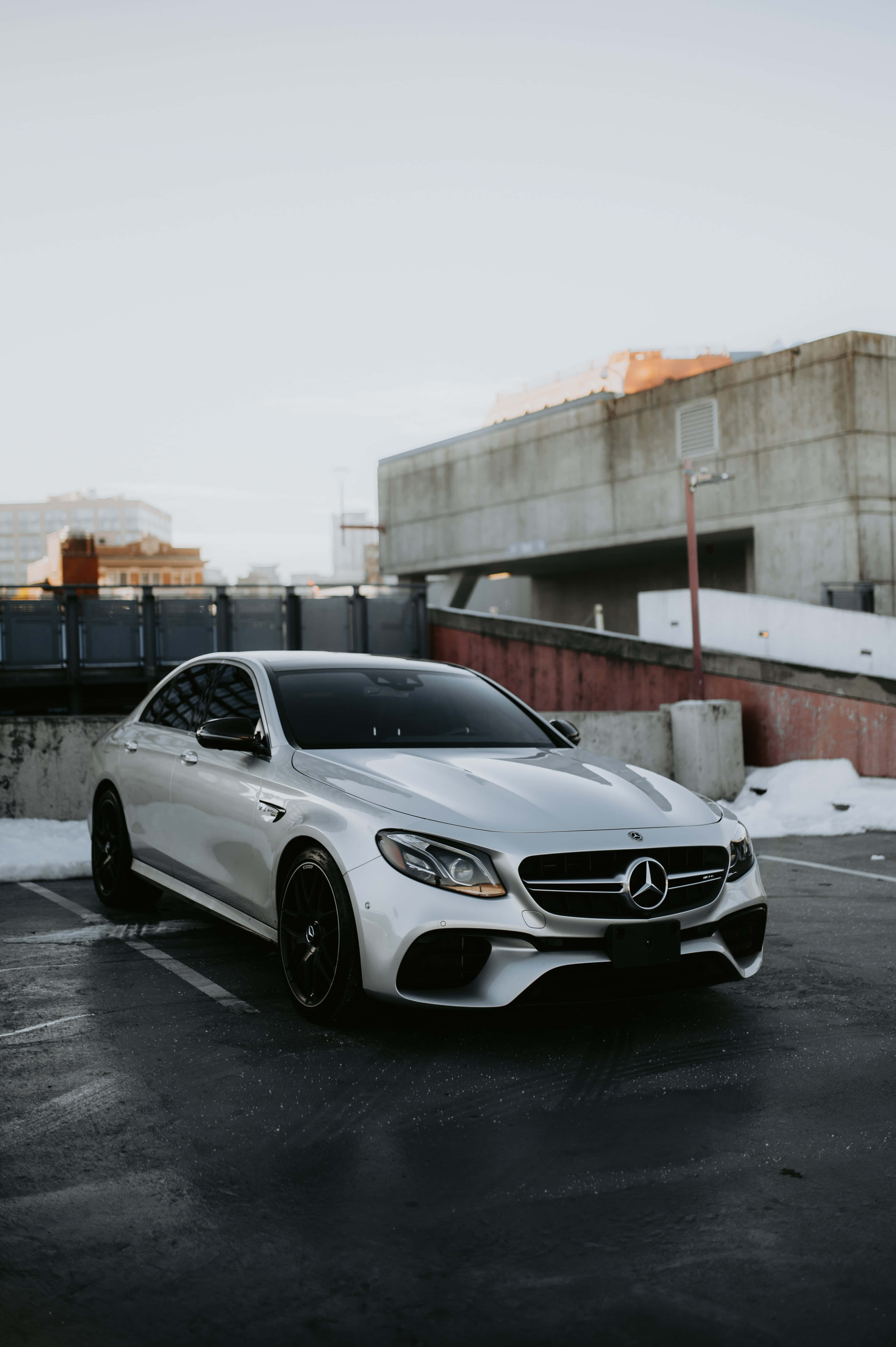 Mercedes 桌布 壁紙 — 一輛時尚的白色Mercedes-AMG停放在積雪的城市停車場，天空多雲。