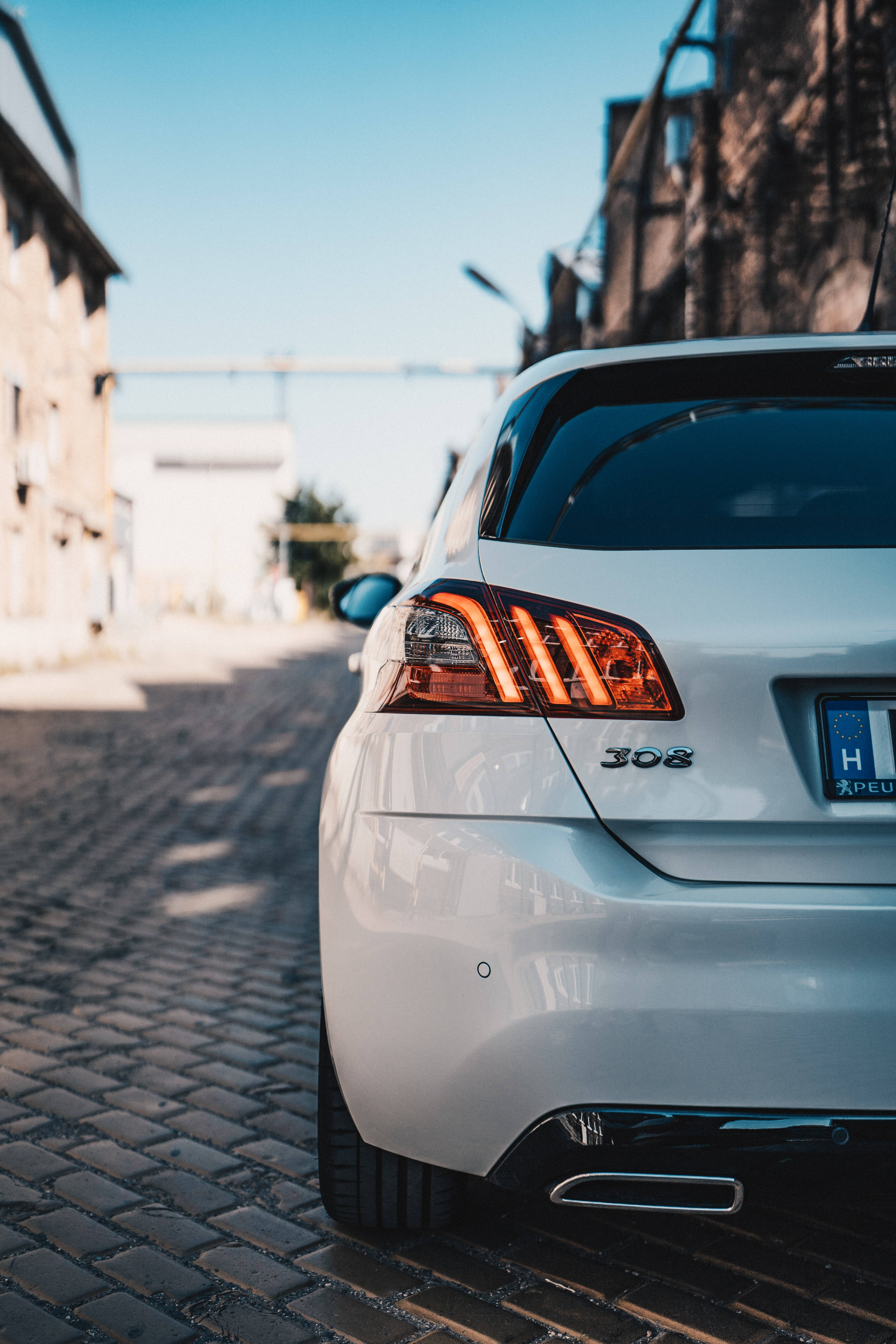 Peugeot 桌布 壁紙 — 一輛時尚的白色Peugeot 308停泊在陽光普照的鵝卵石街道上，背景是歷史建築。