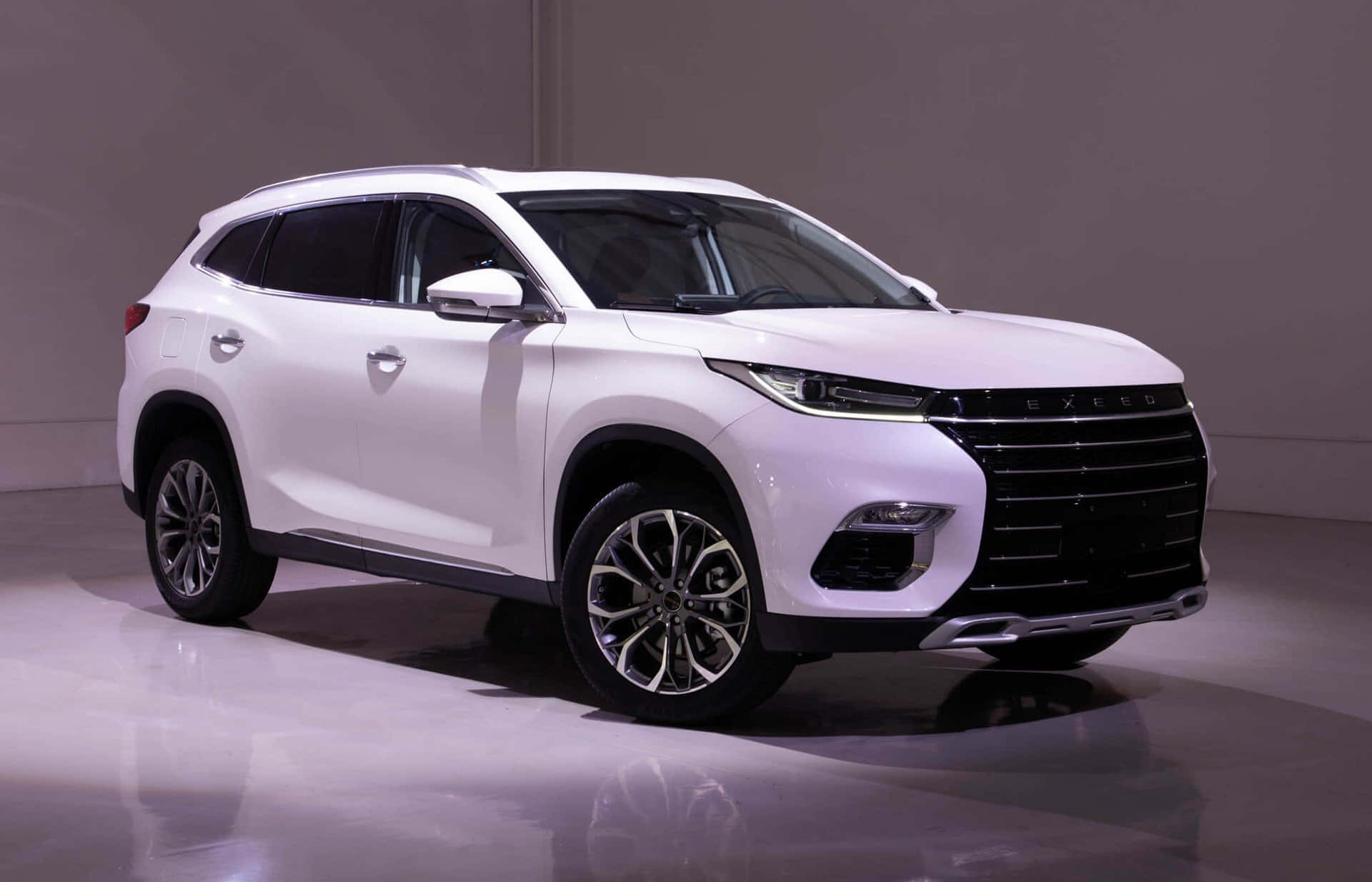 Chery 桌布 壁紙 — 一輛時尚的白色SUV，帶有鍍鉻裝飾和現代頭燈，在攝影棚燈光下展示在反光地板上。