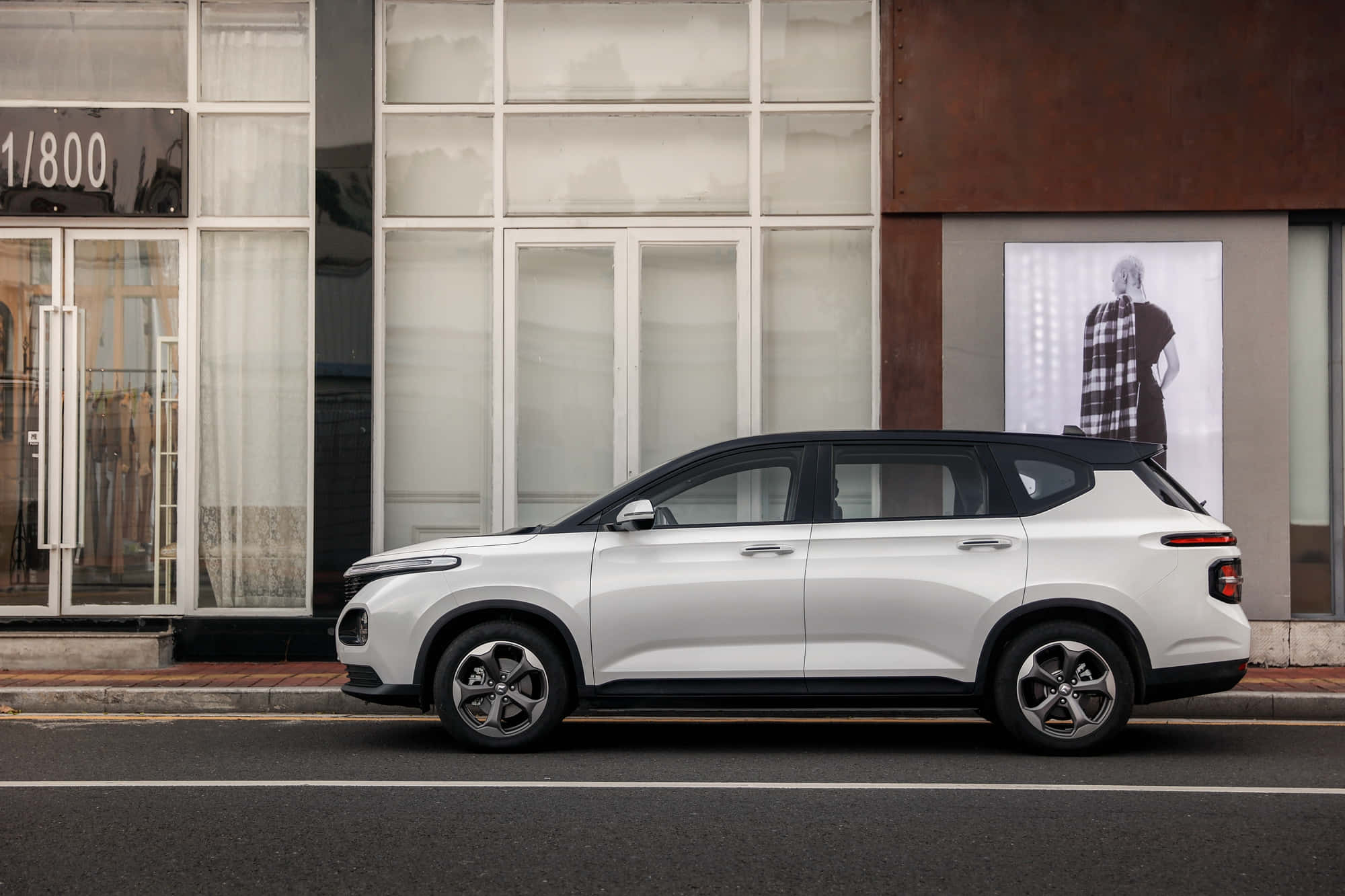 Baojun 桌布 壁紙 — 一輛時尚的白色SUV停放在城市街道上，旁邊是一座帶有大玻璃窗和時尚海報的現代建築。
