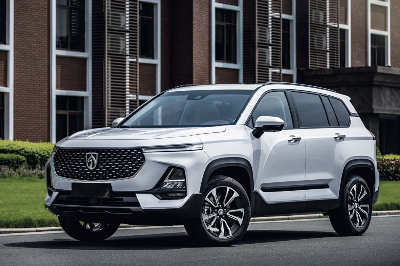 Baojun 桌布 壁紙 — 一輛時尚的白色SUV停放在現代磚砌建築前的瀝青路面上，周圍有綠色灌木。