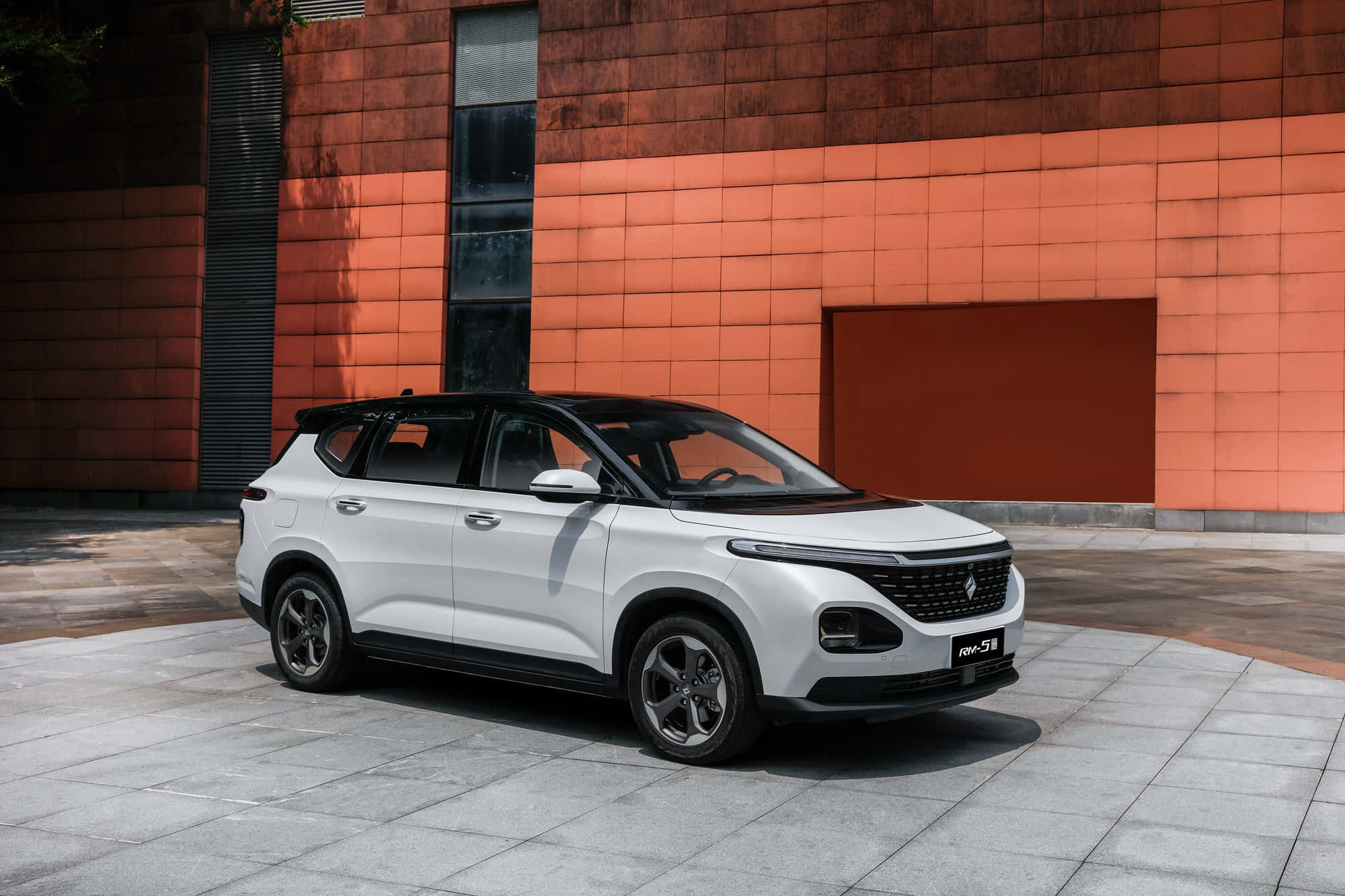 Baojun 桌布 壁紙 — 一輛時尚的白色SUV停泊在瓷磚路面上，背景是一座大膽的橙色磚砌建築，在明亮的日光下。