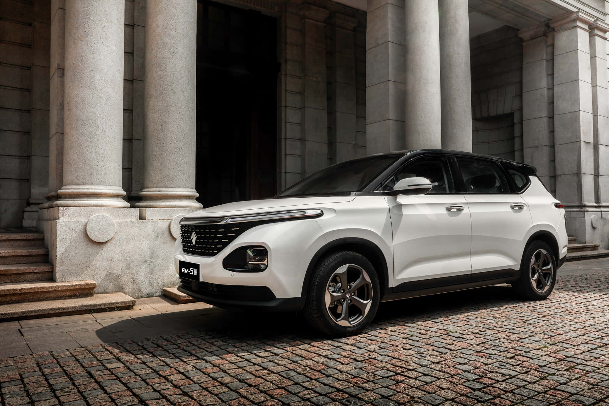 Baojun 桌布 壁紙 — 一輛時尚的白色SUV停泊在鵝卵石街道上，前方是宏偉的石柱建築。