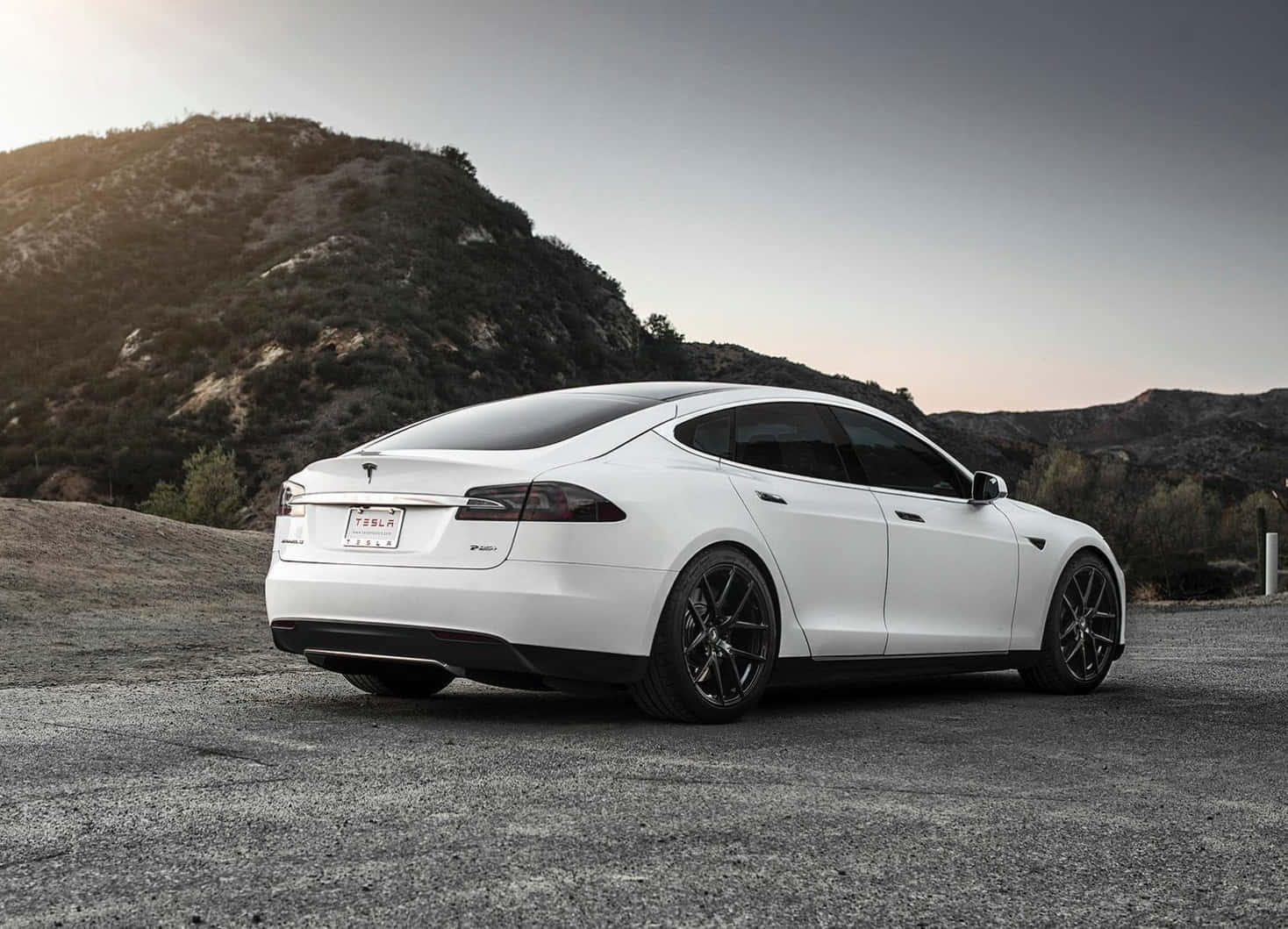 Tesla Model 3 桌布 壁紙 — 一輛時尚的白色Tesla Model S停泊在碎石上，背景是崎嶇的山丘，天空呈現柔和暮色。