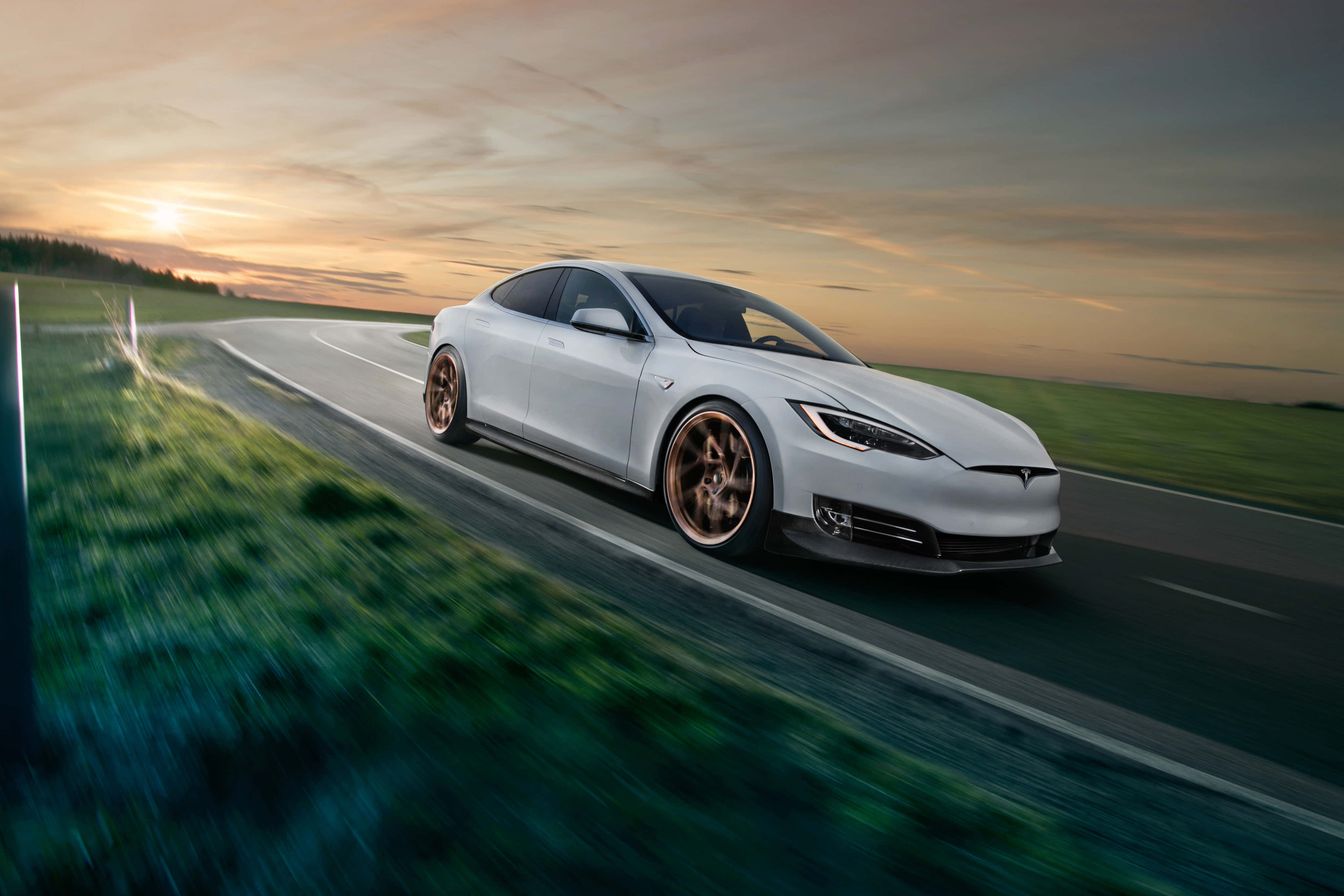 特斯拉 桌布 壁紙 — 一輛時尚的白色Tesla Model S配備青銅輪圈，在日落時分沿著蜿蜒的道路疾馳，背景是模糊的綠色田野。