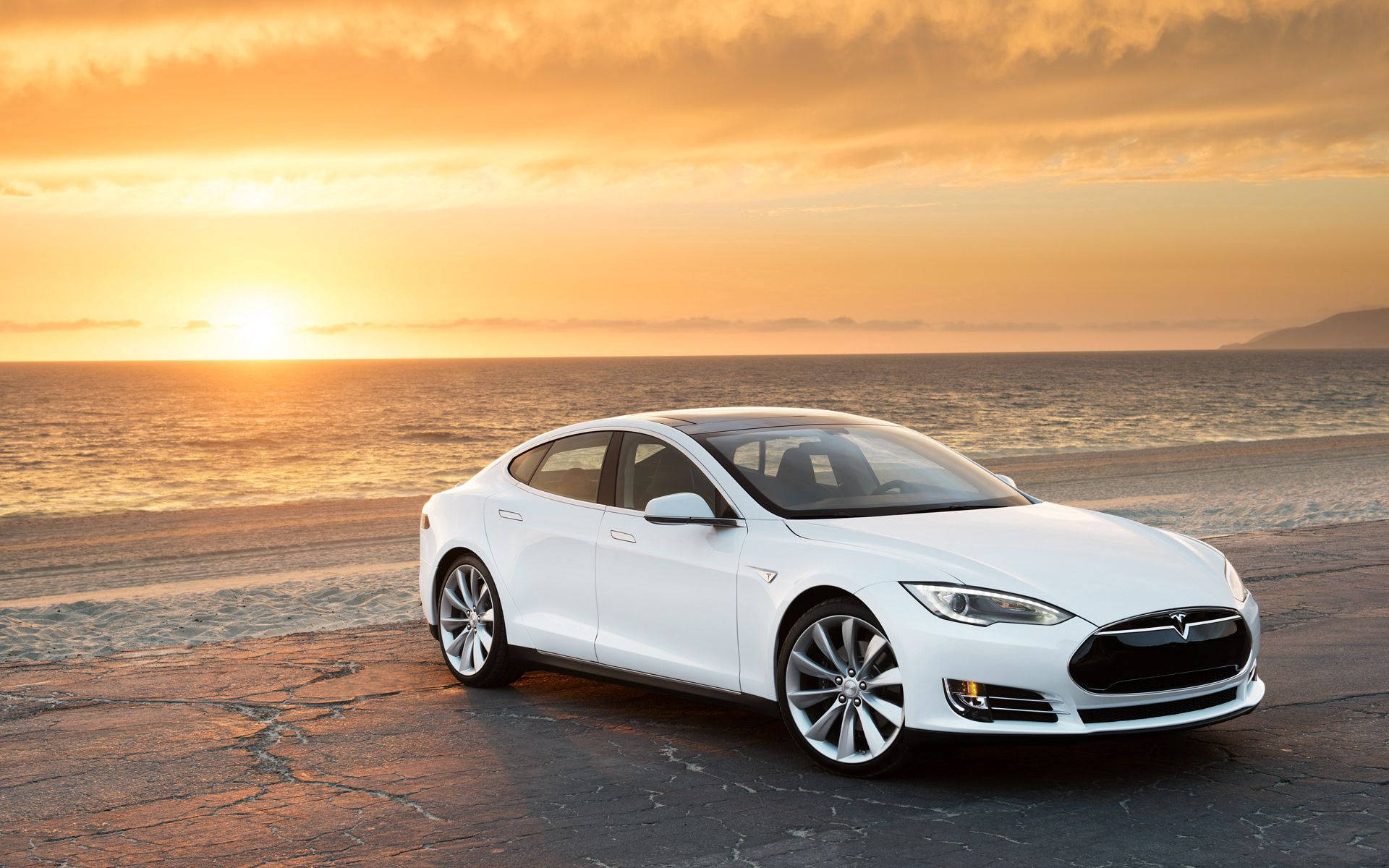 特斯拉 桌布 壁紙 — 一輛時尚的白色Tesla Model S停在日落時分的裂縫路面上，背景是金色的天空和海洋波浪。