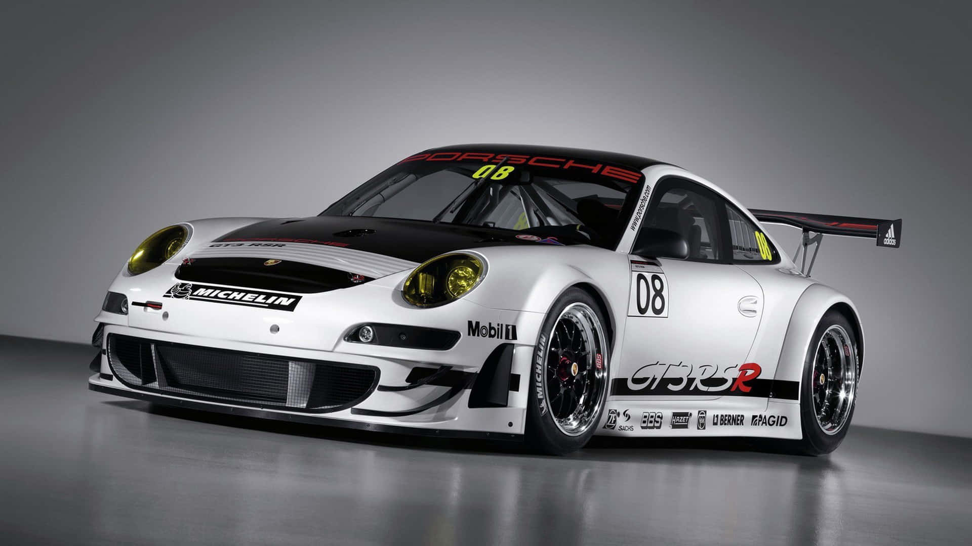 保時捷 桌布 壁紙 — 一輛時尚的白色保時捷911 GT3 R賽車，帶有黑色飾件和贊助商標誌，在反射地板和灰色背景的攝影棚中展示。