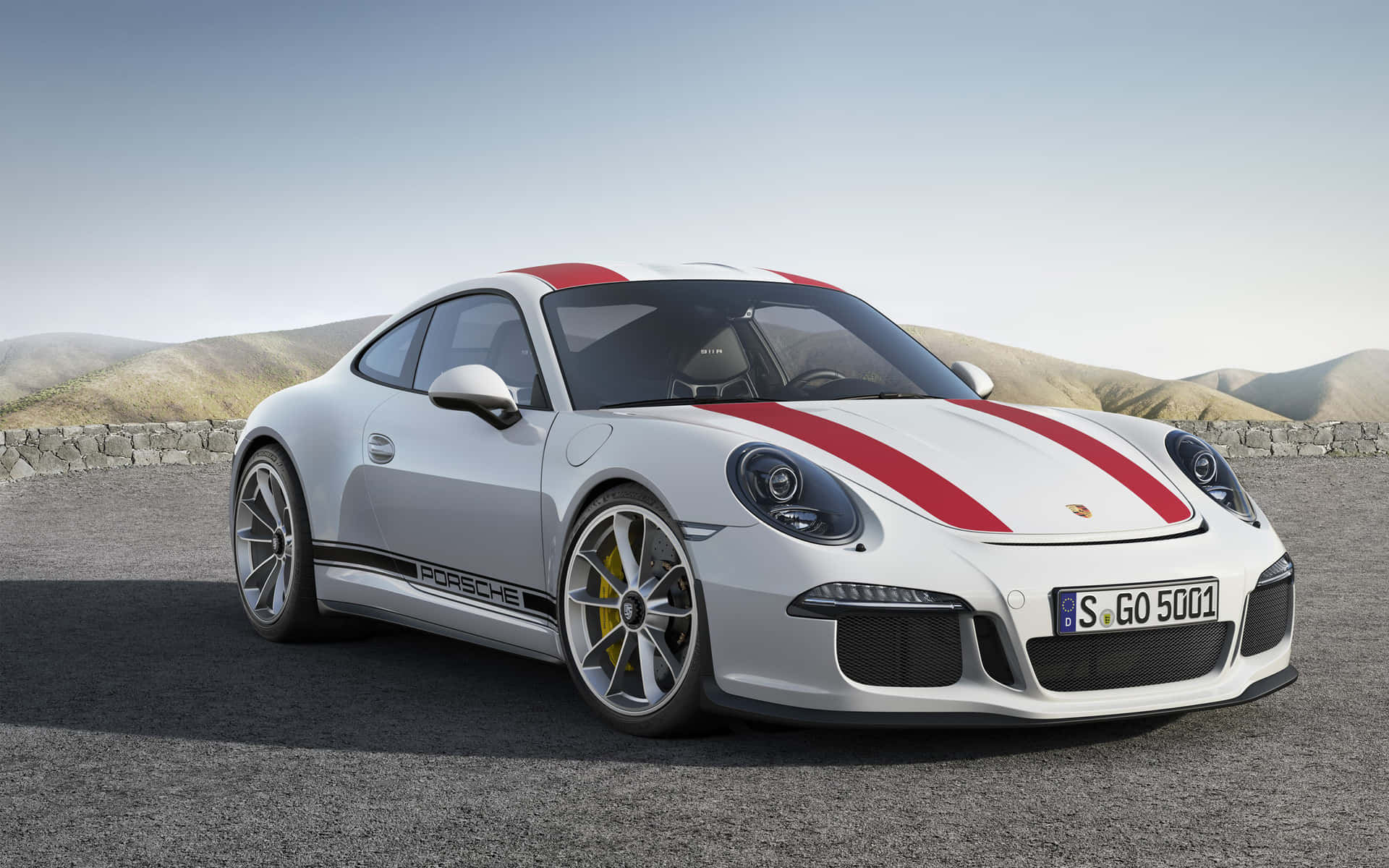 保時捷 桌布 壁紙 — 一輛時尚的白色保時捷911 GT3 RS，帶有醒目的紅色賽車條紋，停在碎石路上，背景是起伏的丘陵，天空晴朗。