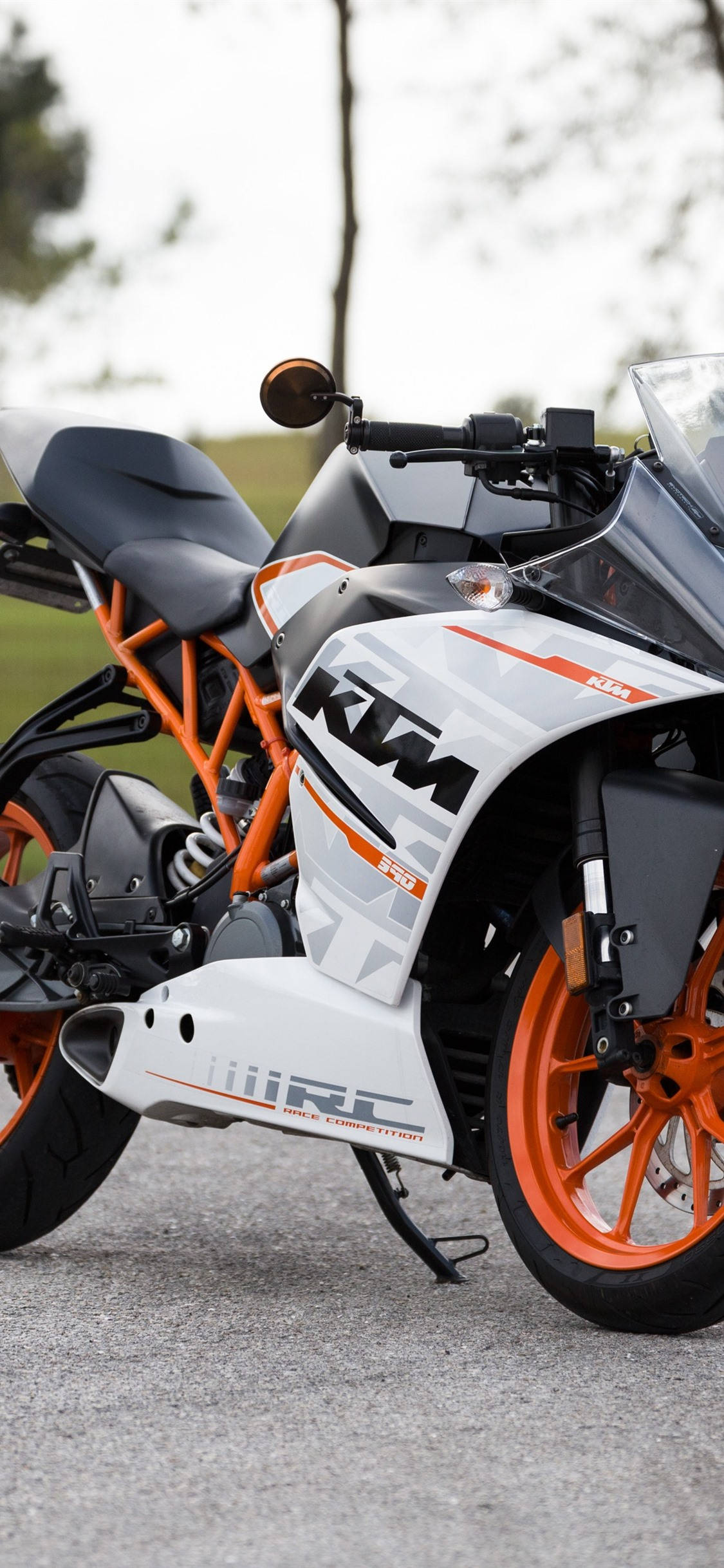 機車 桌布 壁紙 — 一輛時尚的白色和橙色KTM RC摩托車停在柏油路上，背景有柔和的樹木。