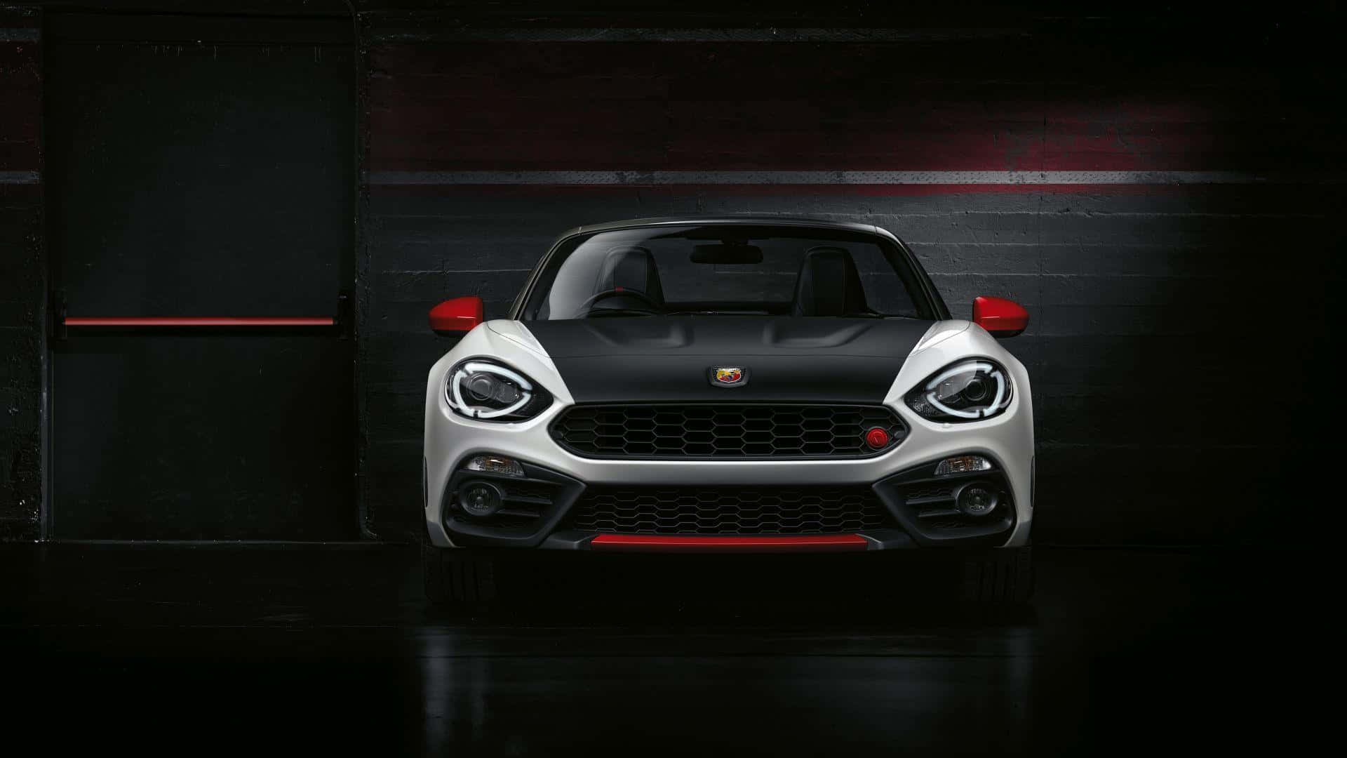 Abarth 桌布 壁紙 — 一輛時尚的白色和黑色Fiat 124 Spider，帶有紅色點綴，在黑暗的車庫中被戲劇性地照亮，展示其侵略性的前臉設計。