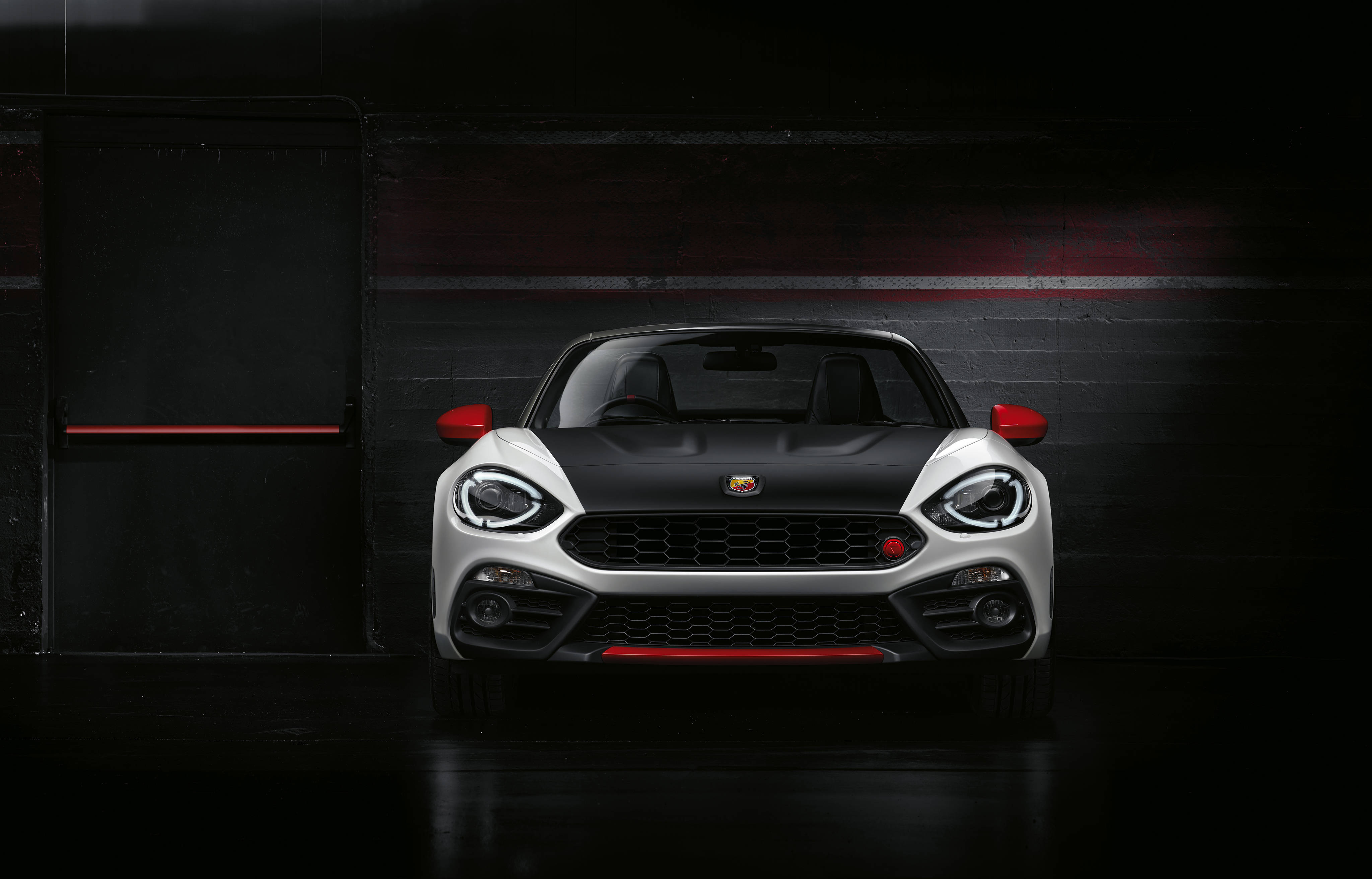 Fiat 桌布 壁紙 — 一輛時尚的白色和黑色菲亞特124 Spider，帶有紅色點綴，在黑暗的工業車庫中被戲劇性地照亮。