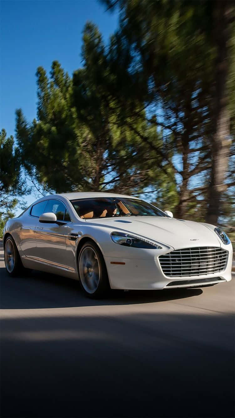 Aston Martin Rapide S 桌布 壁紙 — 一輛時尚的白色奧斯頓馬丁在陽光明媚的道路上奔馳，道路兩旁綠樹成蔭，頭頂是清澈的藍天。