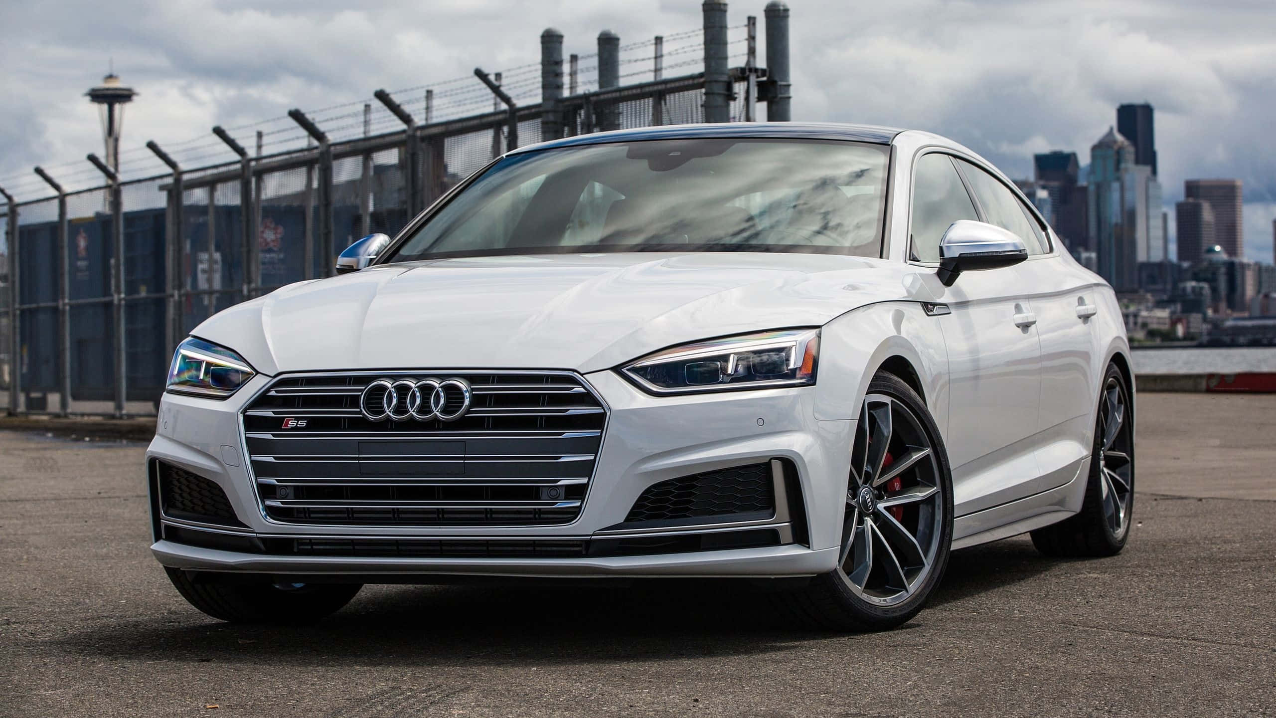 Audi S5 桌布 壁紙 — 一輛時尚的白色奧迪RS5雙門跑車停在海濱，背景是西雅圖天際線和太空針塔，天空多雲。