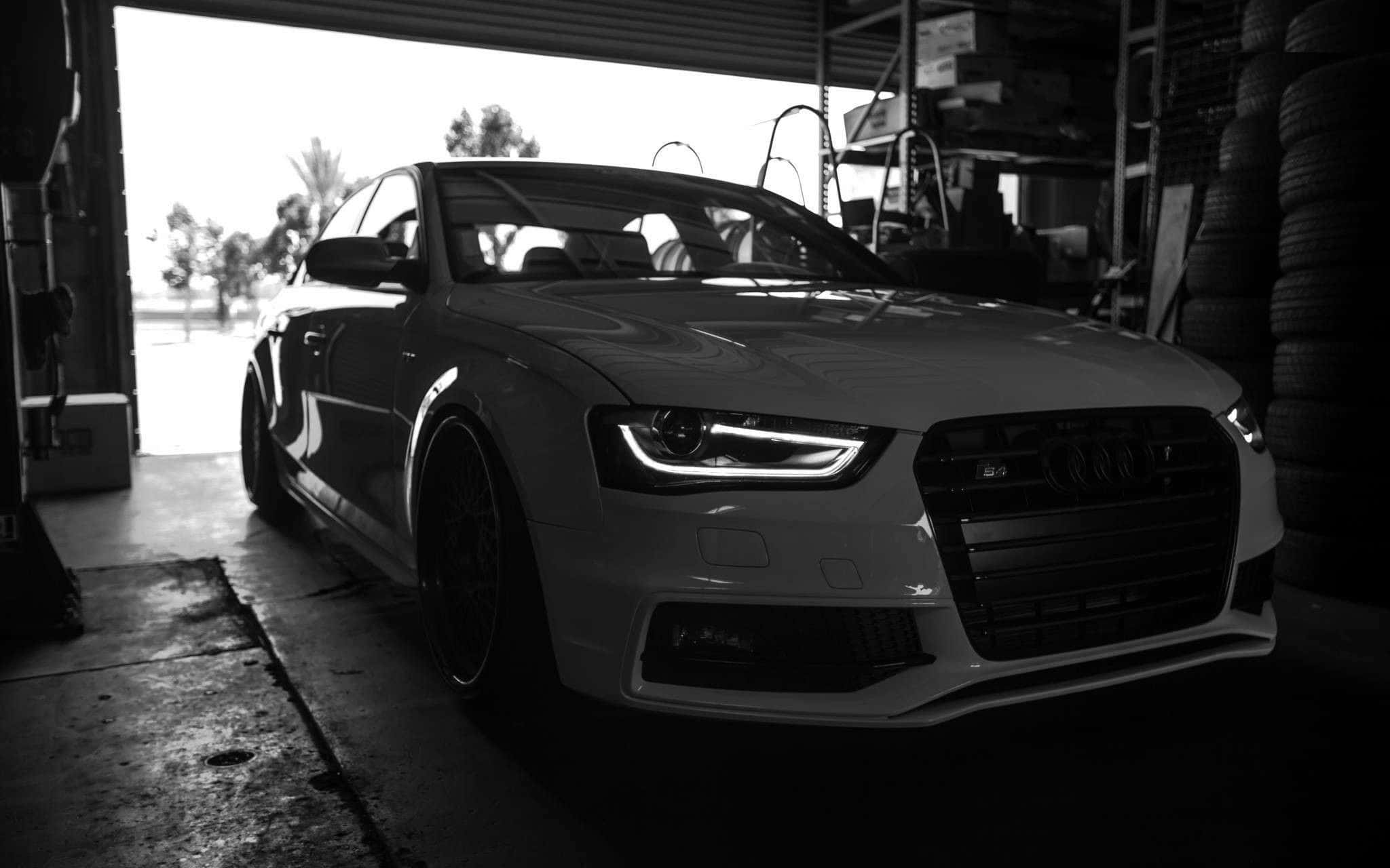 Audi S4 桌布 壁紙 — 一輛時尚的白色奧迪S5停放在光線昏暗的車庫中，附近堆疊著輪胎，明亮的日光從敞開的門照射進來。