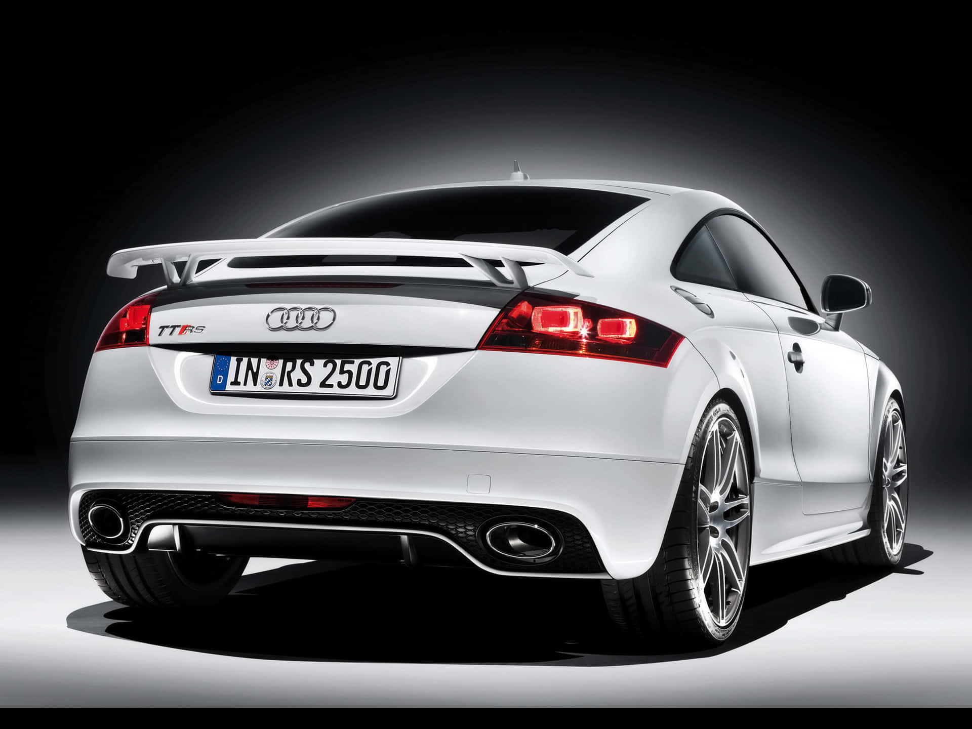 Audi Tt Rs 桌布 壁紙 — 一輛時尚的白色奧迪TT RS跑車從後方觀看，帶有發光的紅色尾燈和突出的擾流板，背景為深色工作室。