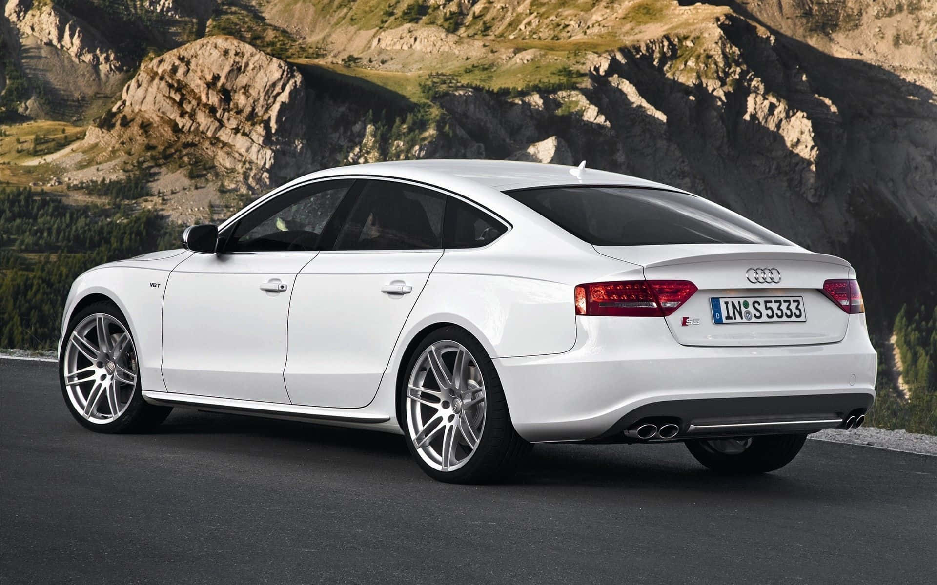 Audi S5 桌布 壁紙 — 一輛時尚的白色奧迪轎車停在山路上，背景是崎嶇的懸崖和綠意。