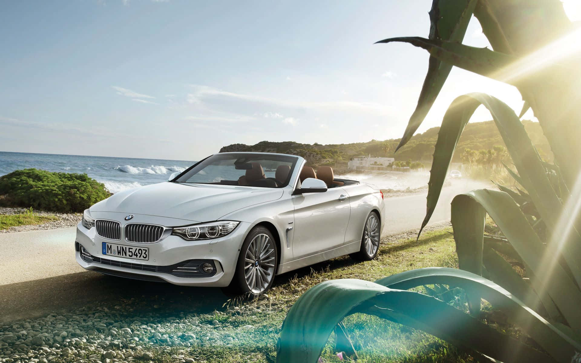 Bmw 4 Series 桌布 壁紙 — 一輛時尚的白色寶馬敞篷車停放在沿海公路上，附近有海浪拍打，陽光穿過熱帶樹葉灑落。