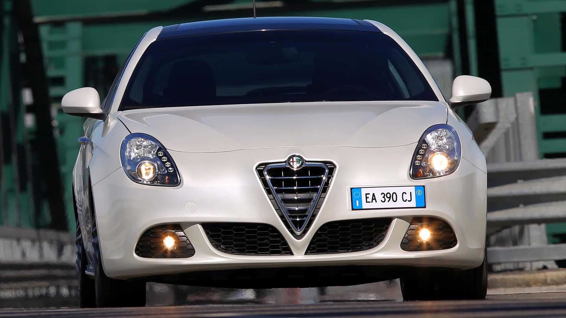 Alfa Romeo Giulietta 桌布 壁紙 — 一輛時尚的白色愛快羅密歐跑車，配備發光頭燈，在明亮的日光下朝前停在潮濕的賽道上。