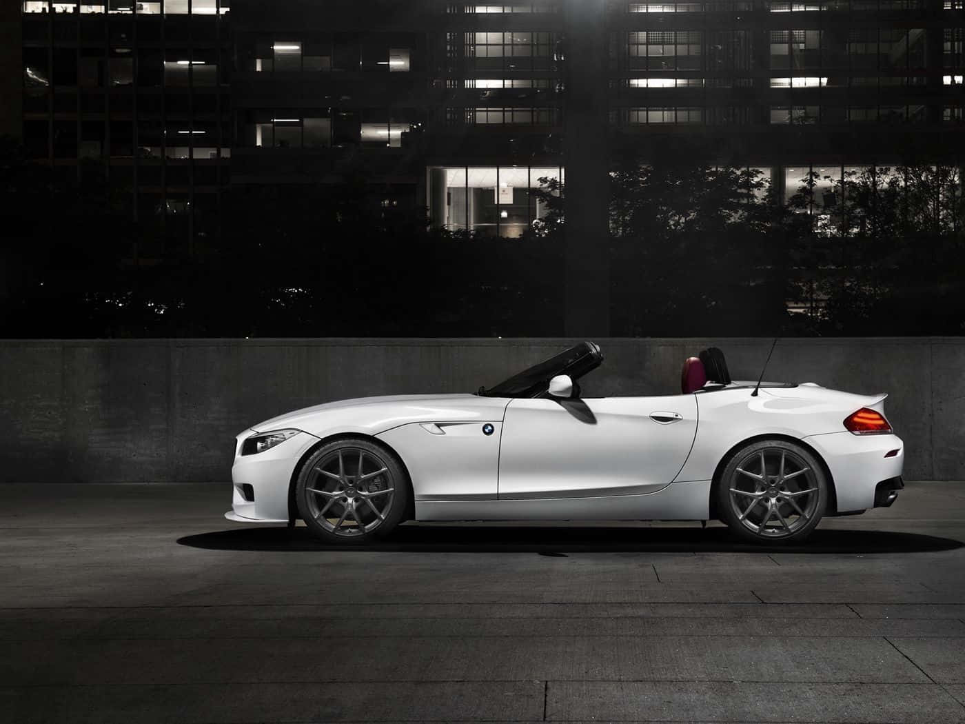 Bmw Z4 桌布 壁紙 — 一輛時尚的白色敞篷跑車在夜晚停泊於燈火通明的城市建築背景下。
